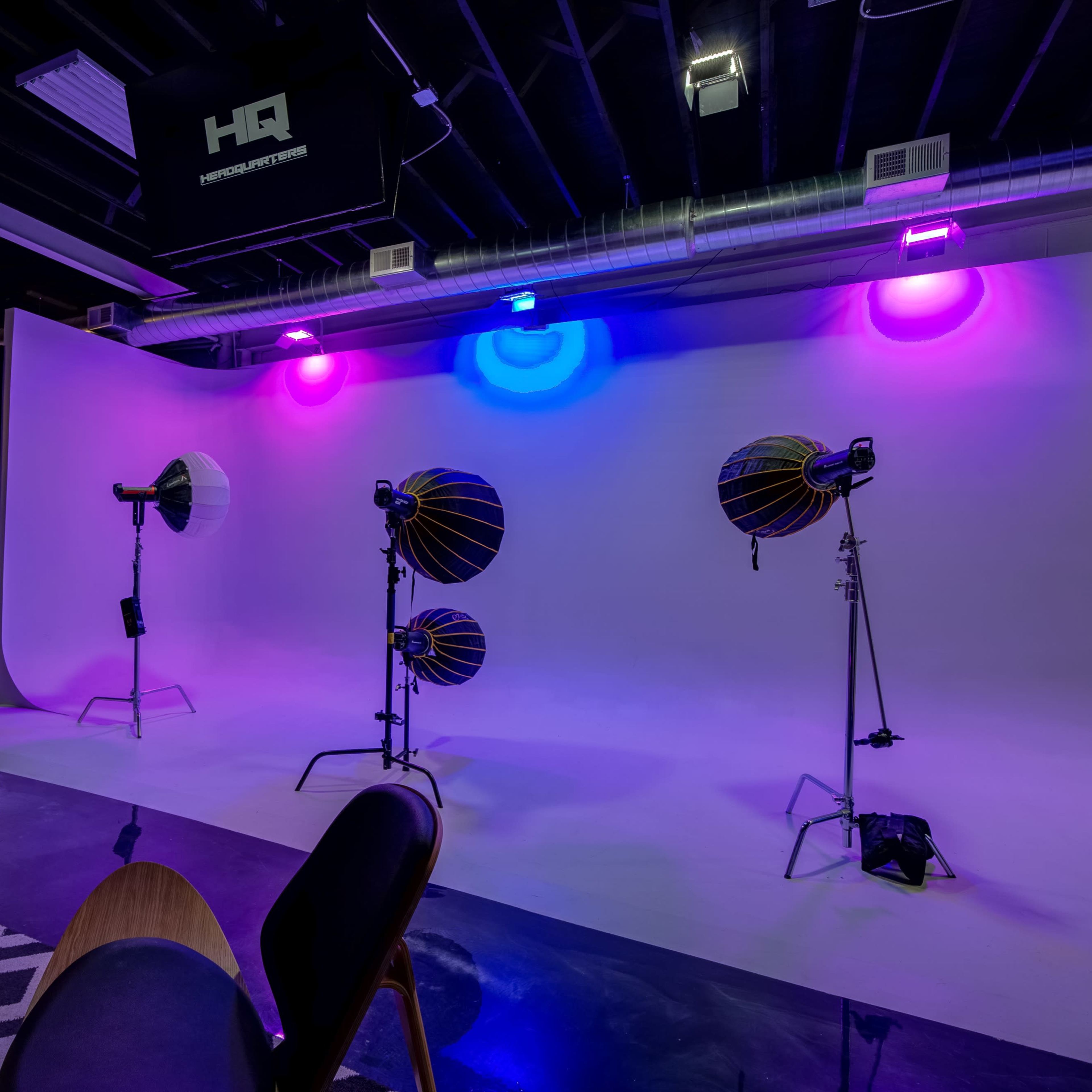 A photography studio set up with a white backdrop, colorful lighting, and several studio lights.