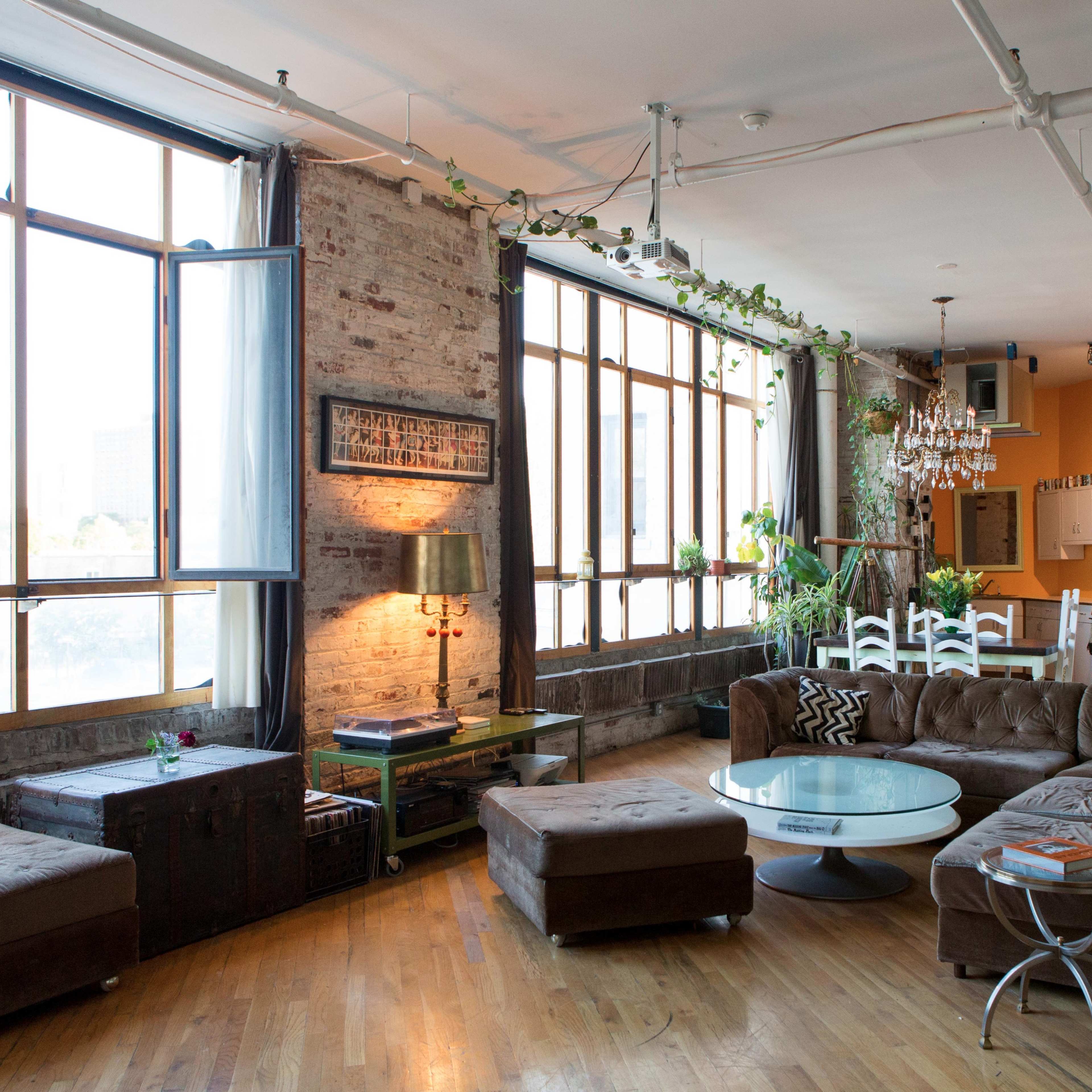 A spacious, modern loft with large windows, a comfortable seating area, and an open kitchen in the background.