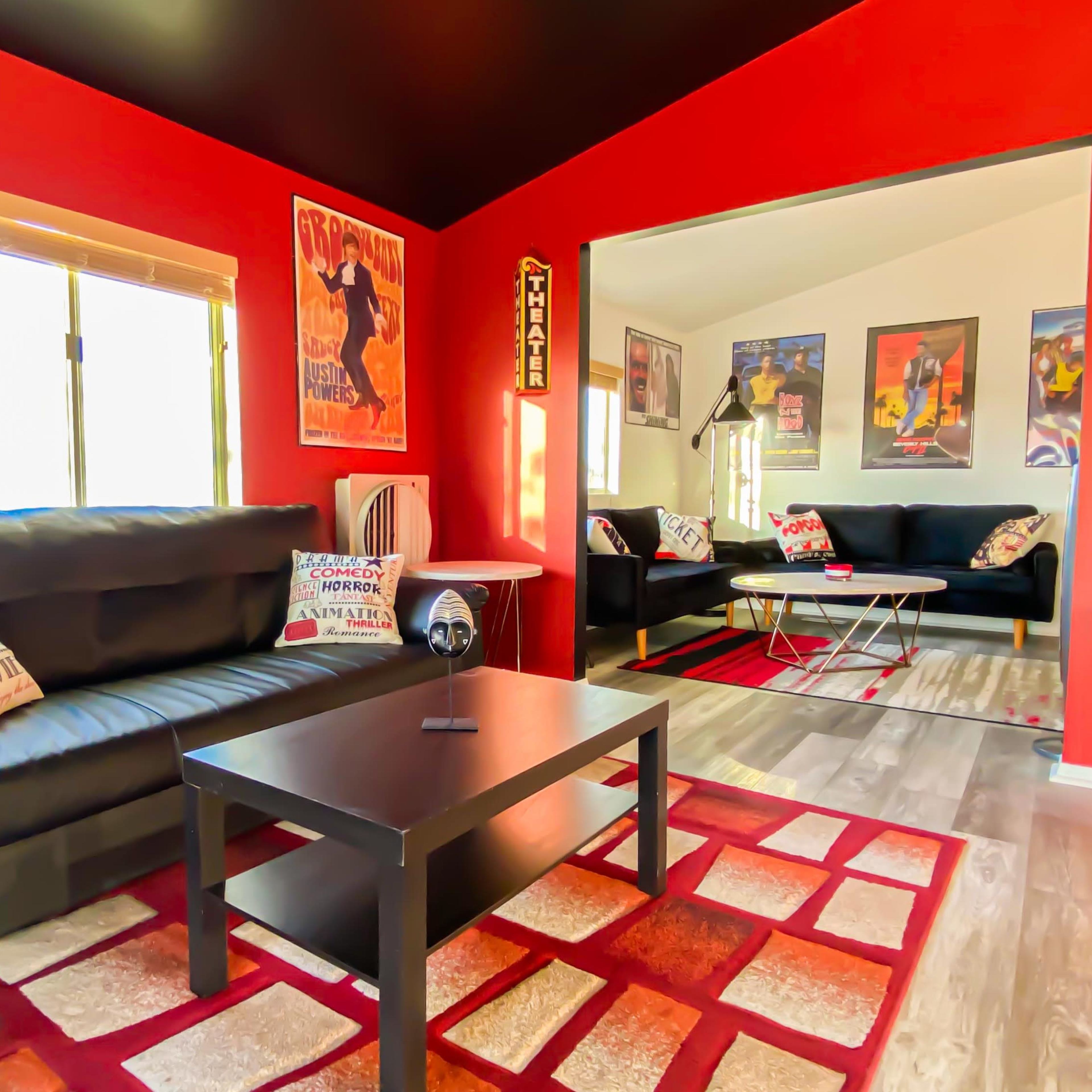 A living room with black leather sofas, a coffee table, and walls adorned with movie posters, set against a red color scheme.