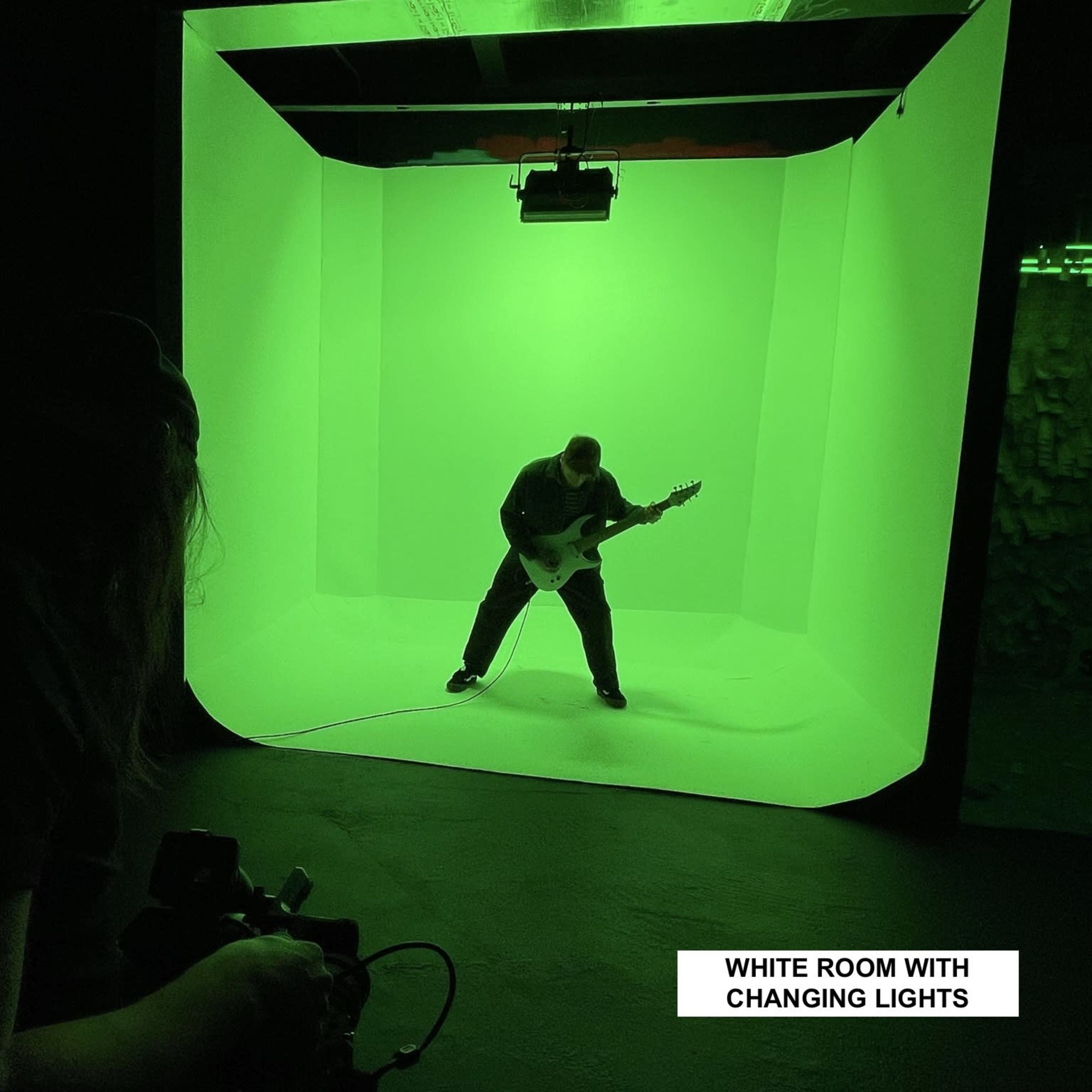 A musician plays an electric guitar in a green-lit studio with a changing light backdrop.