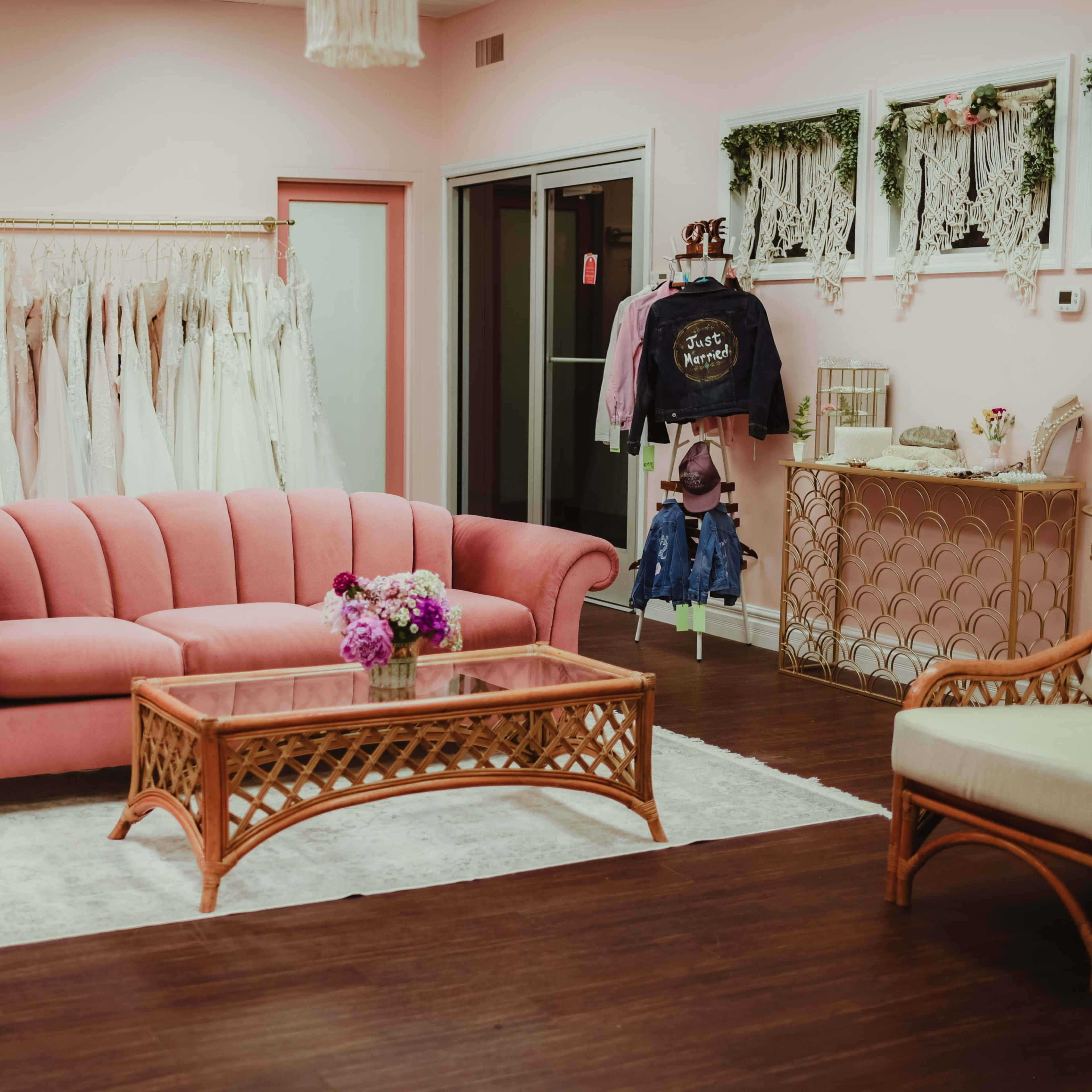 A pink boutique interior with a pink couch, a coffee table, and a rack of wedding dresses in the background.