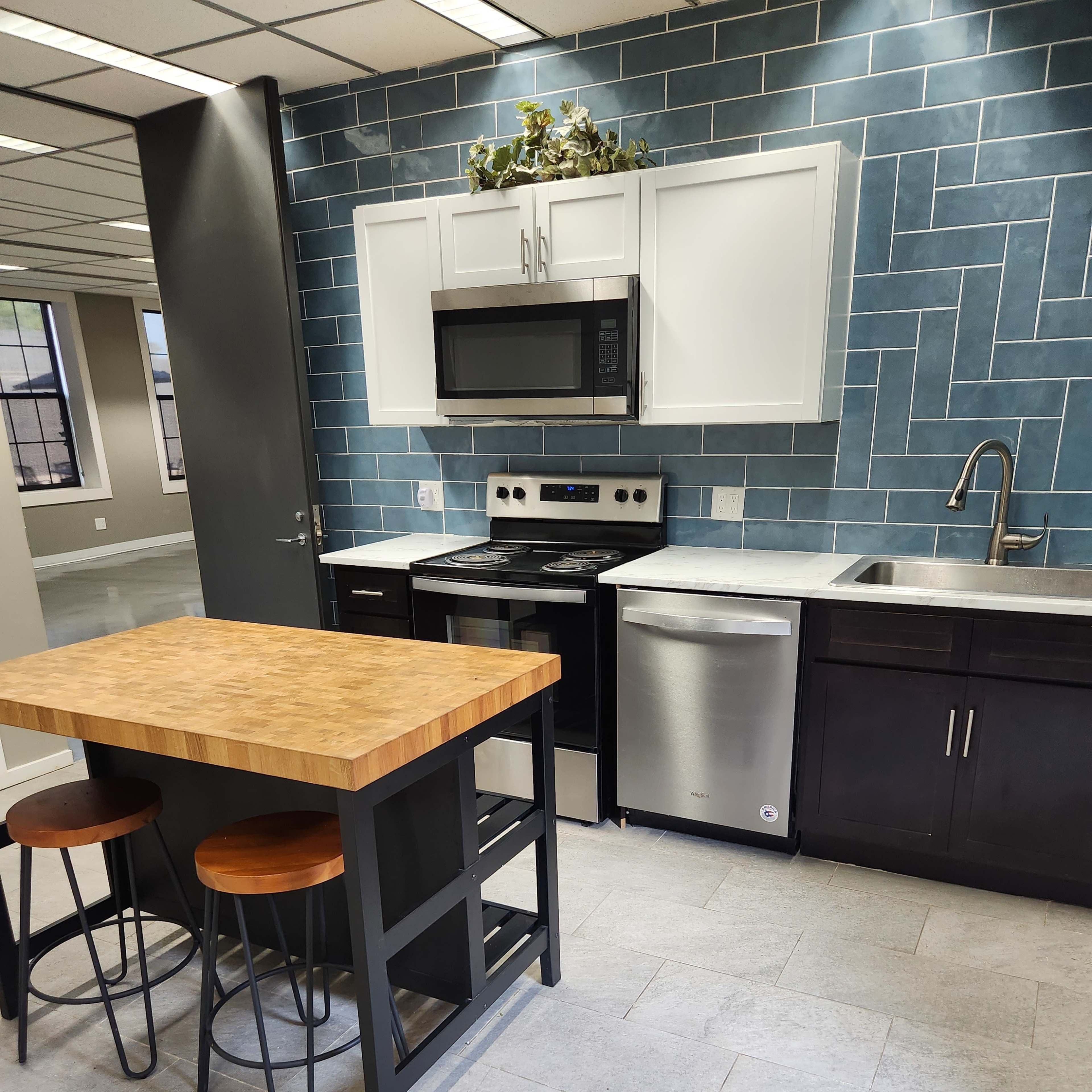 A modern kitchen featuring a blue tiled backsplash, a wooden island with two stools, and stainless steel appliances.