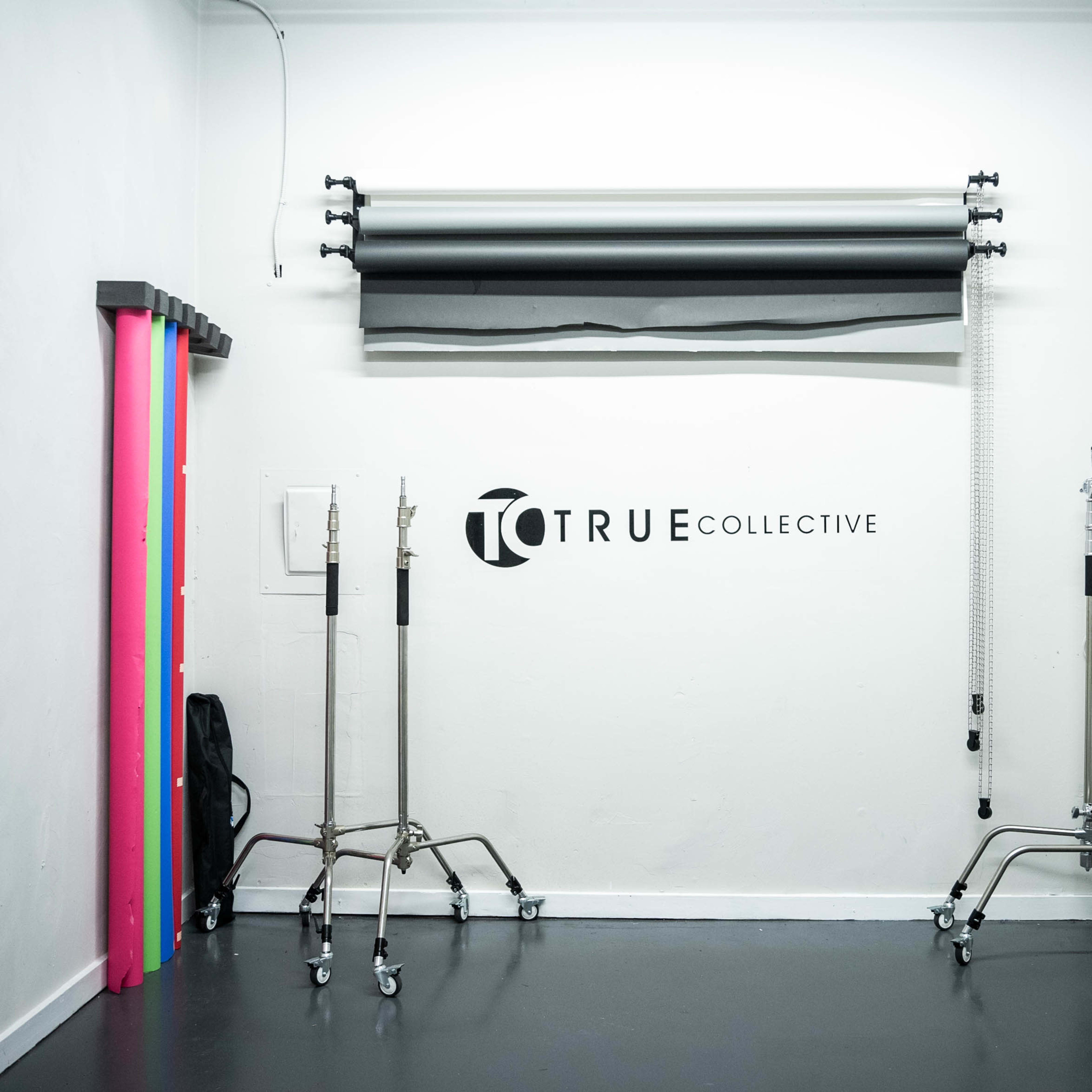 A studio space featuring a wall with the text "TRUE COLLECTIVE," several background roll paper colors, and equipment stands.