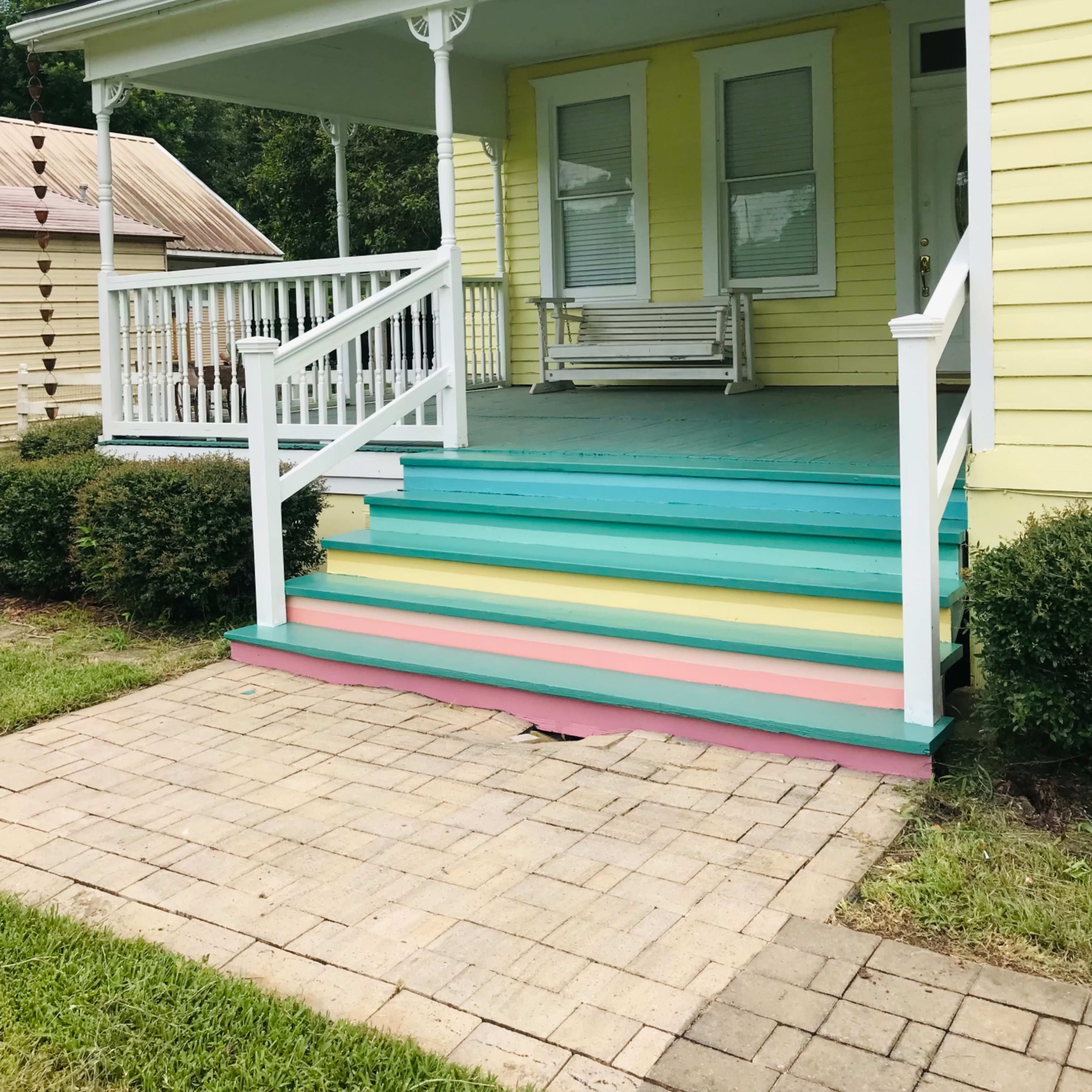 A yellow house with a front porch featuring multicolored steps, flanked by neatly trimmed hedges.