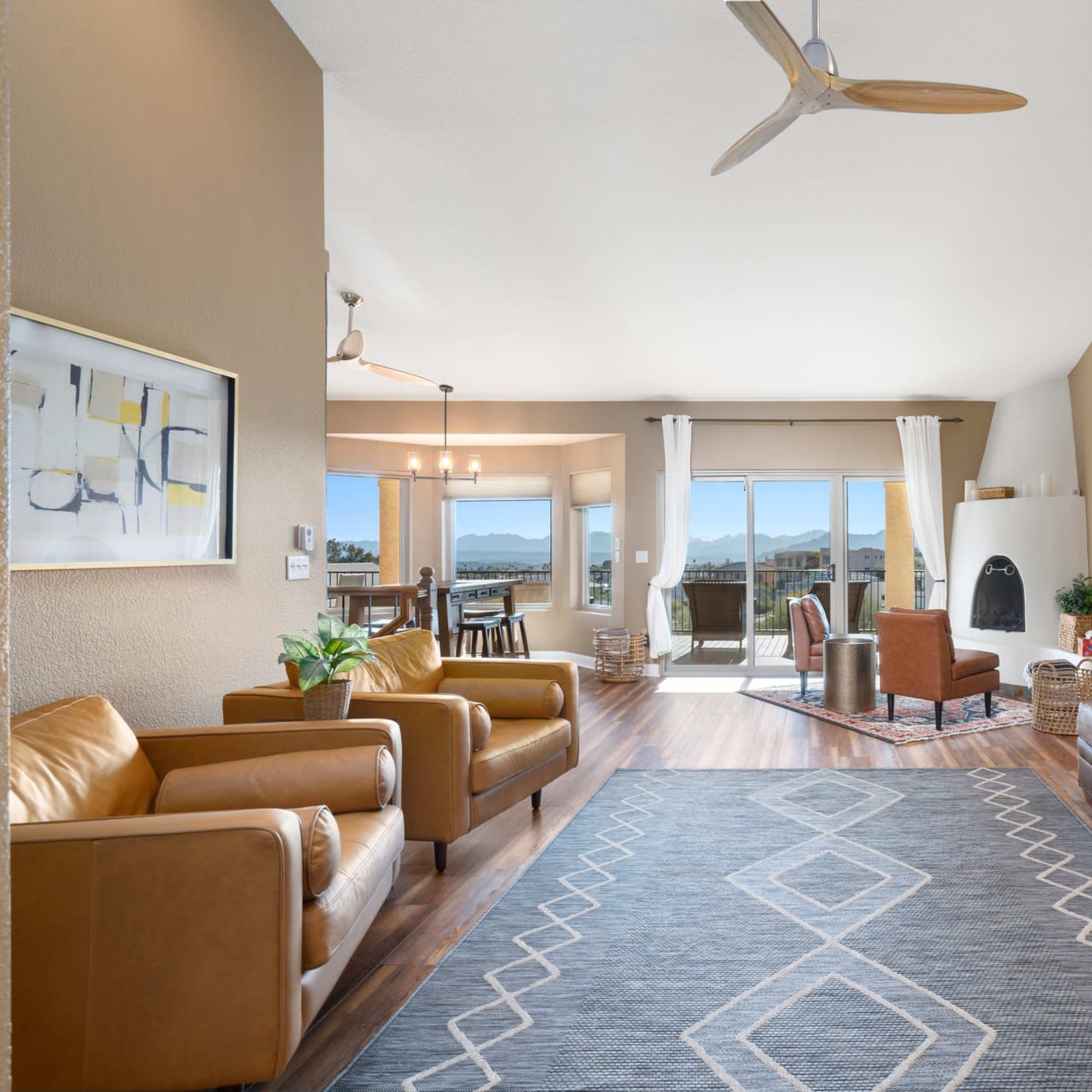 A modern living room with two leather armchairs and a brown leather sofa, a patterned rug on the wooden floor, and large windows revealing a scenic view.