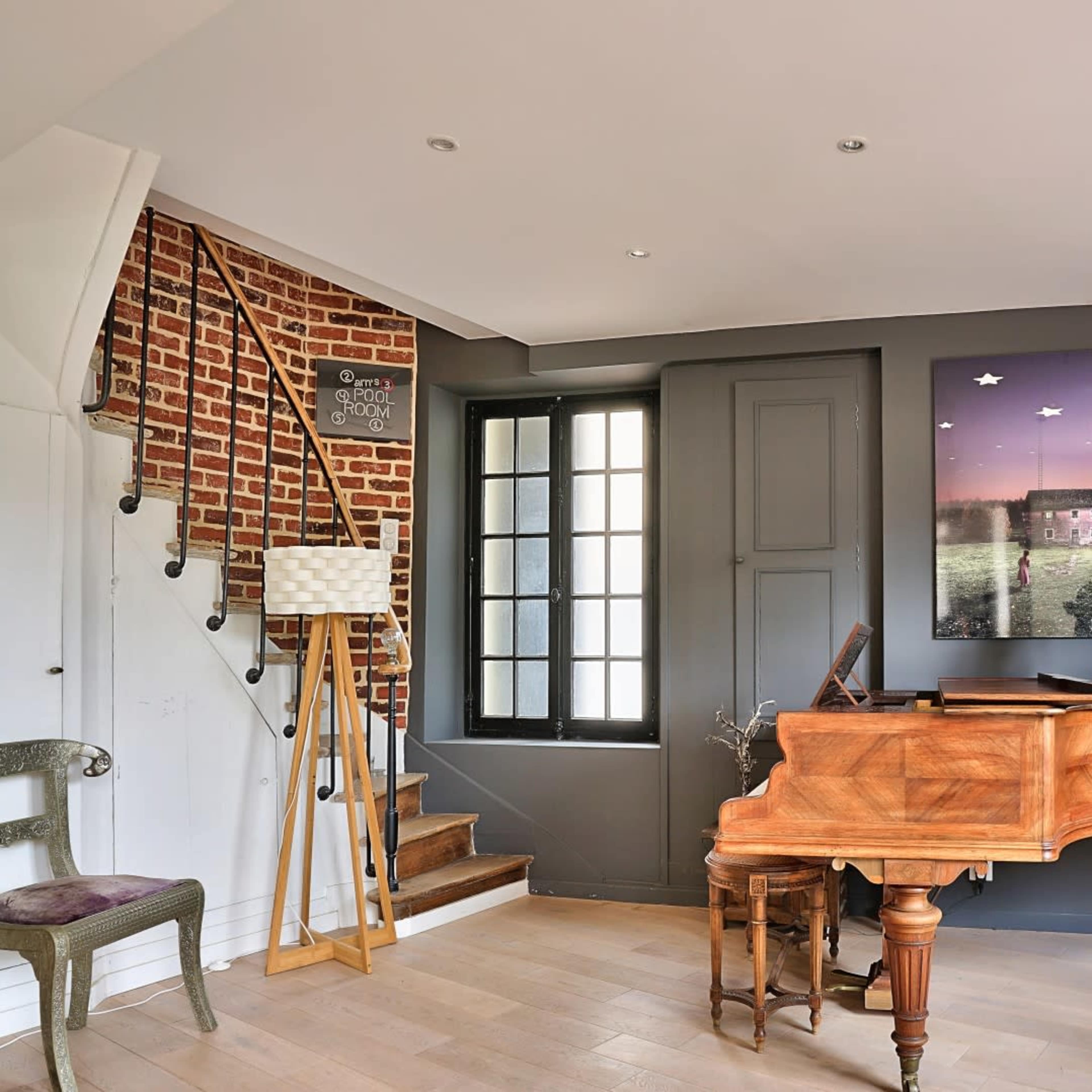 A modern interior featuring a wooden grand piano, a decorative sculpture, and a staircase leading to an upper level.