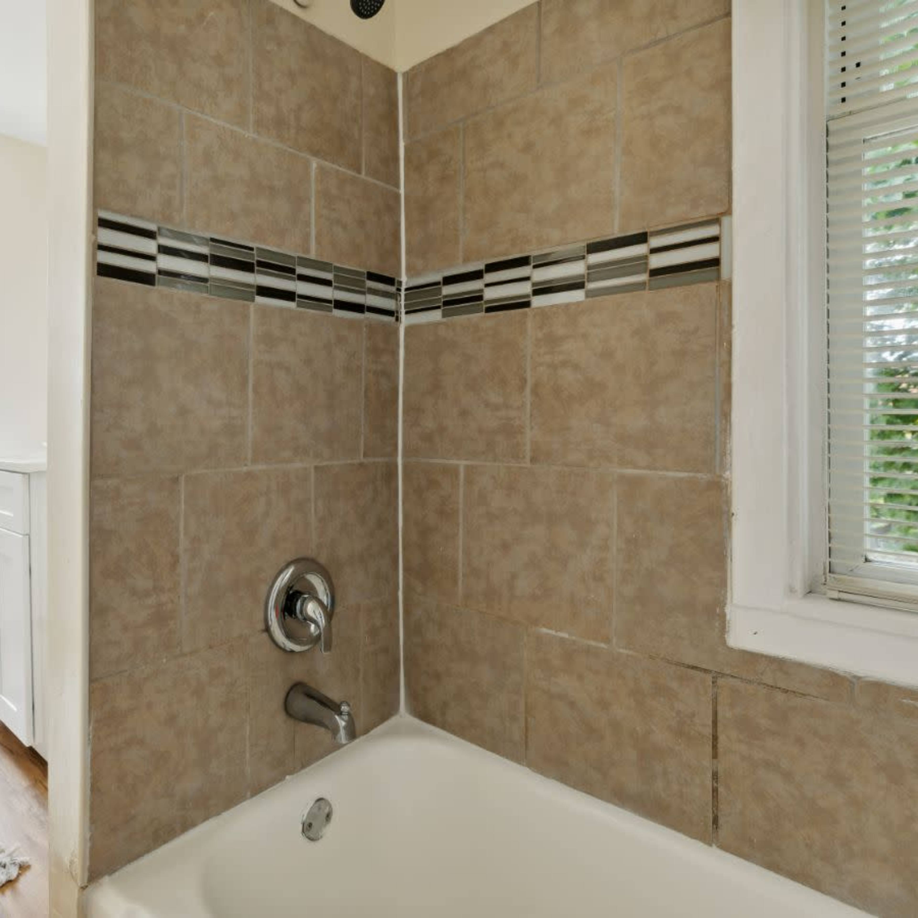 A bathroom with a bathtub, tiled walls, and a window, featuring a showerhead above the tub.