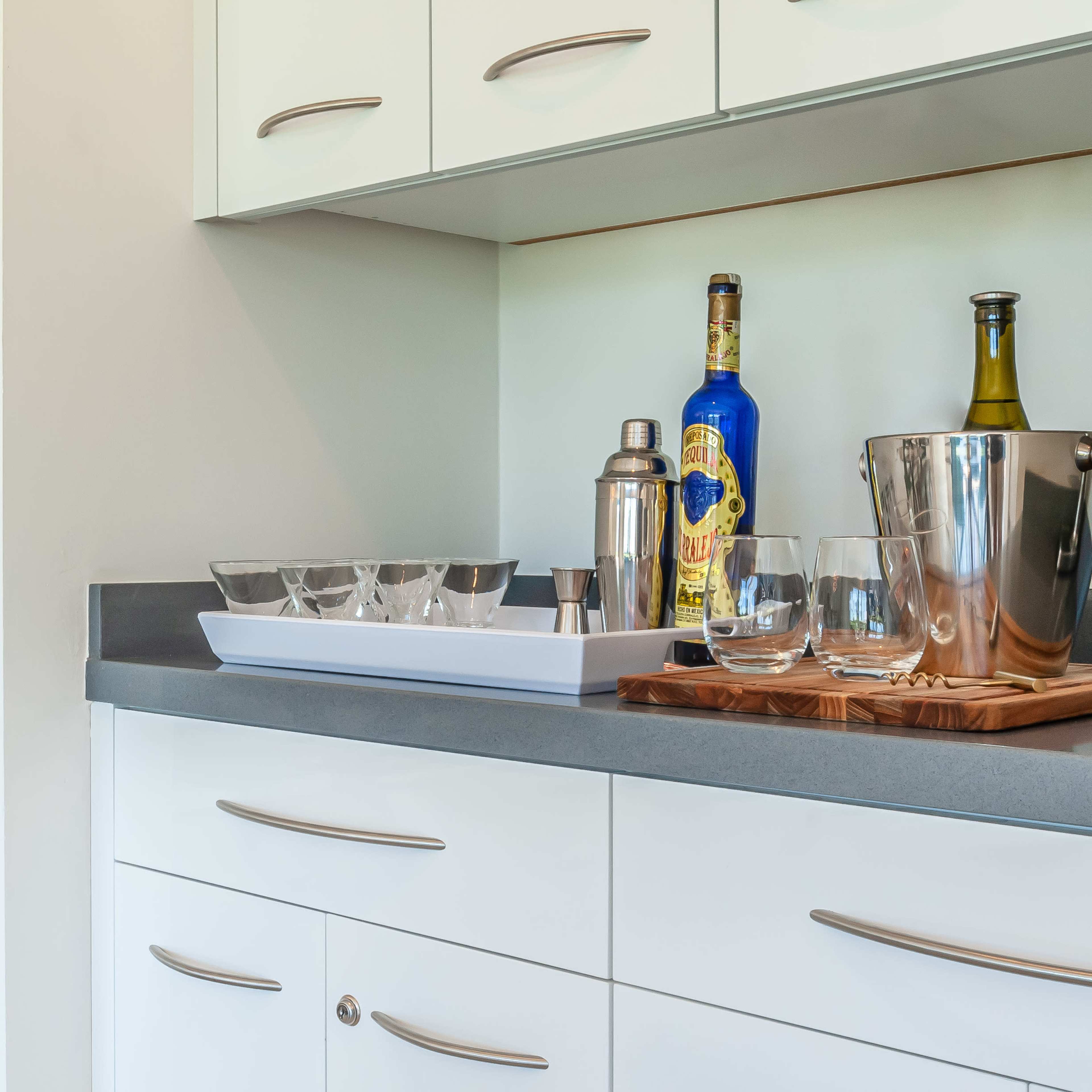 A modern kitchen countertop with a selection of glassware, a cocktail shaker, a bottle, and an ice bucket on display.