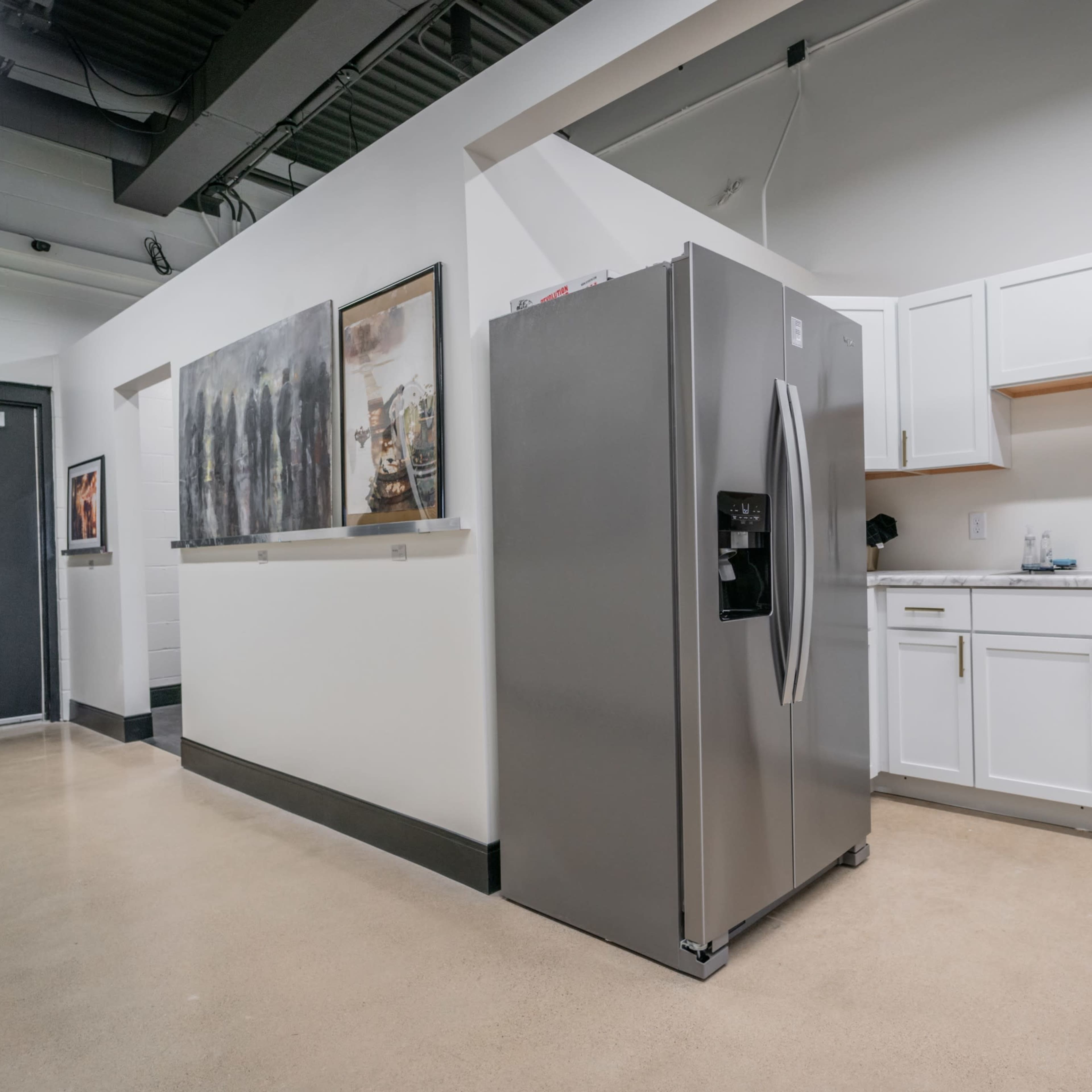 A modern kitchen area featuring stainless steel appliances, white cabinetry, and a smooth concrete floor.
