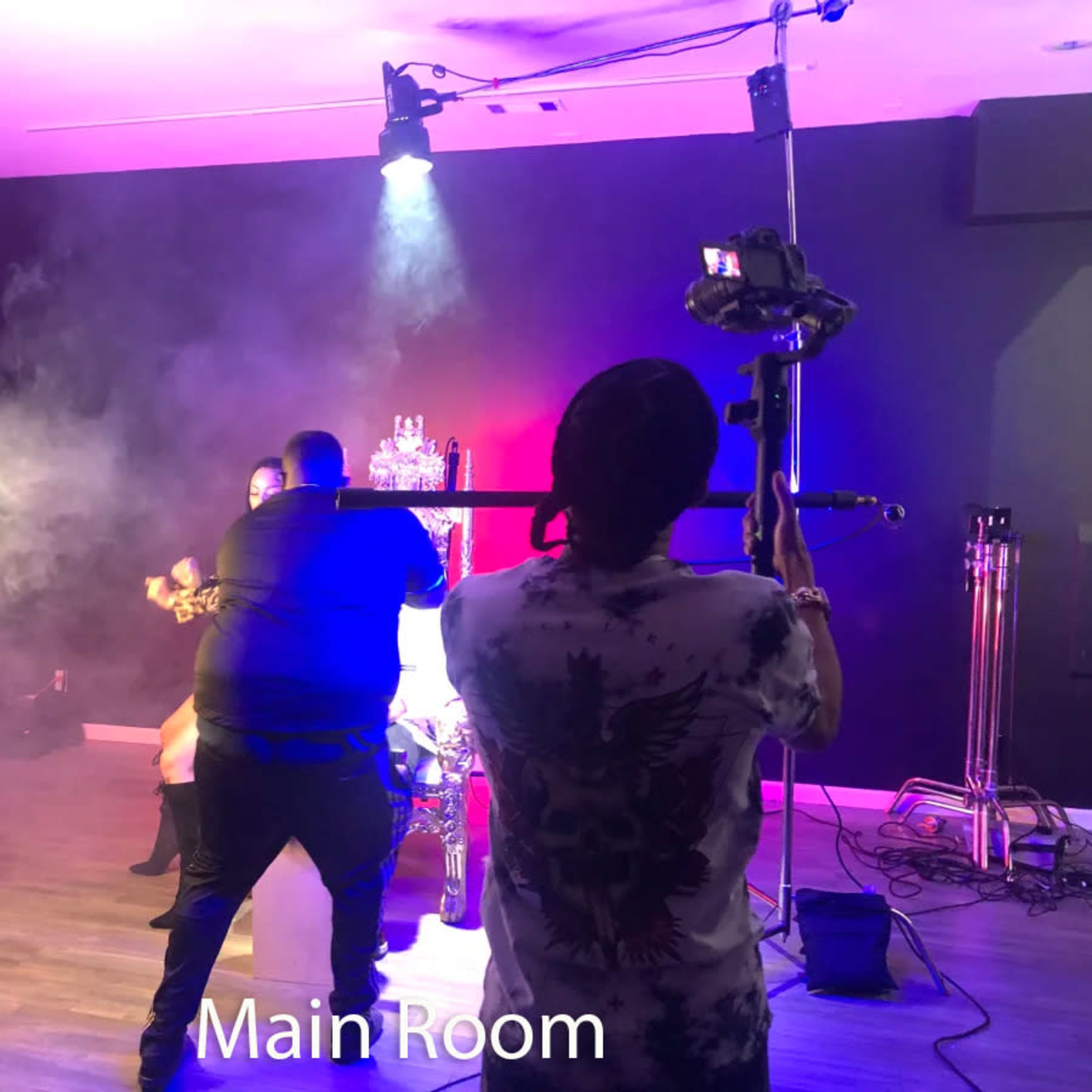 A person is filming a scene in a studio with smoke effects and various lighting setups while another person adjusts the shot.