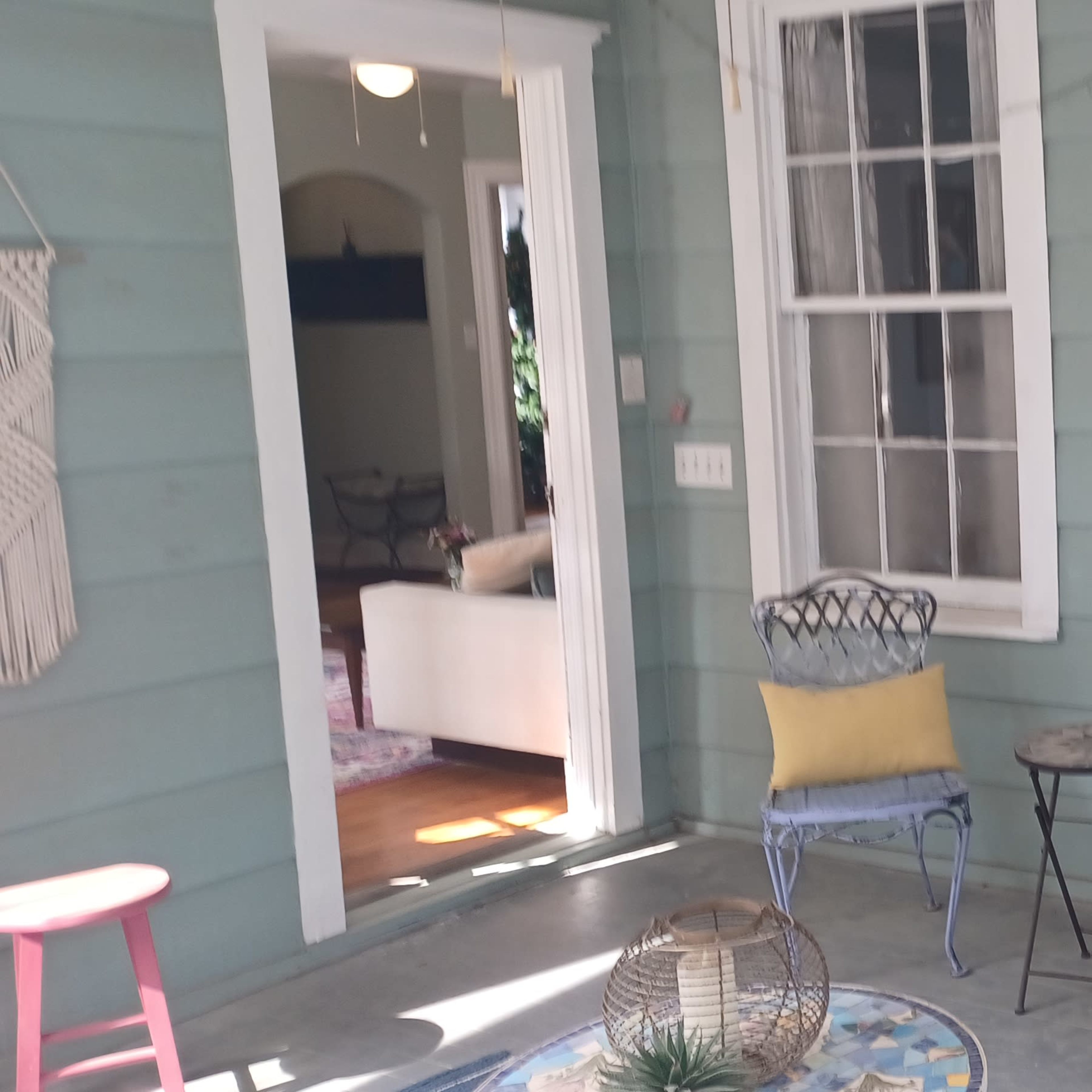 A porch with light green walls, two windowed sides, and a combination of colorful chairs, a small table, and a rocking chair.