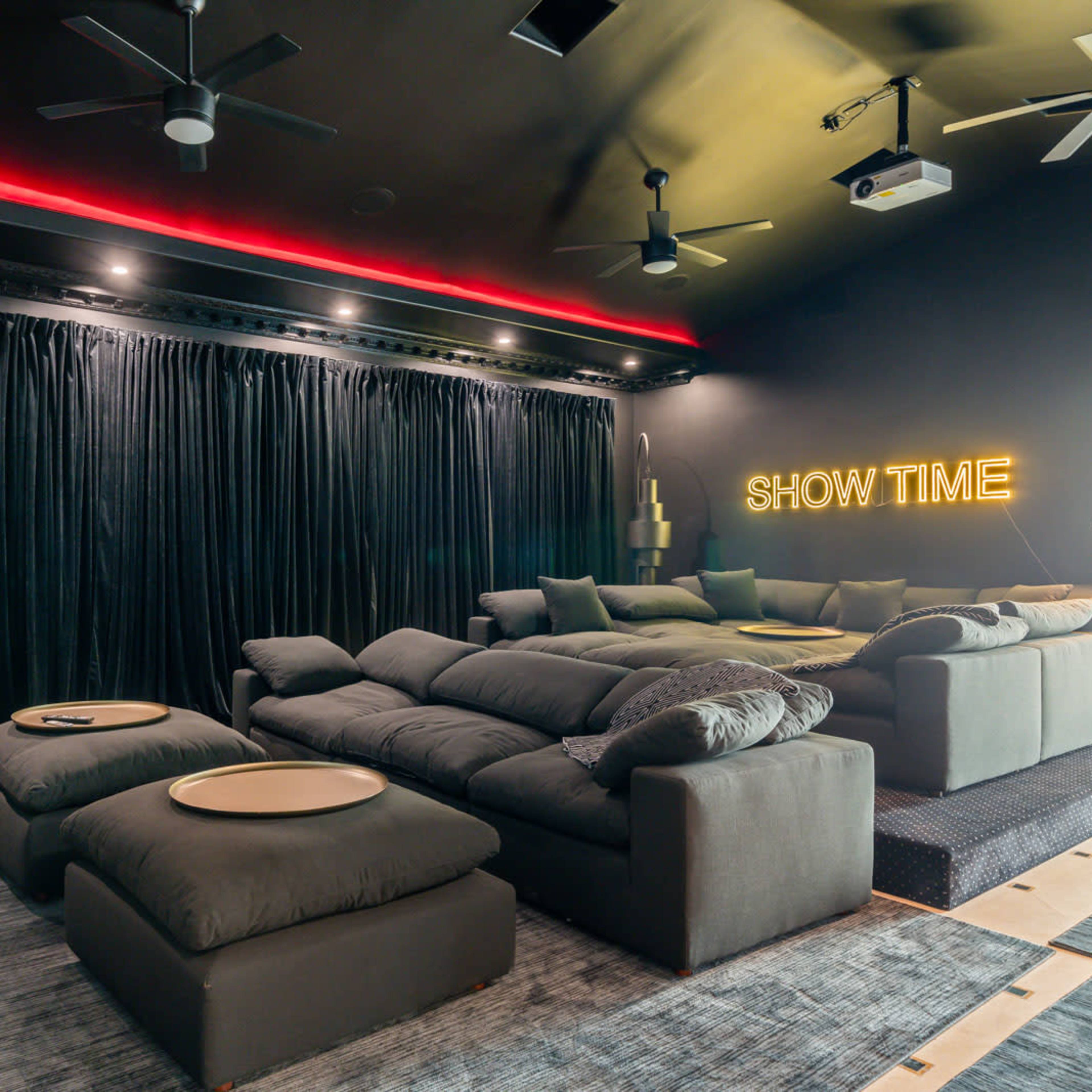 A home theater room with black walls, plush seating, and a neon sign that reads "SHOW TIME."