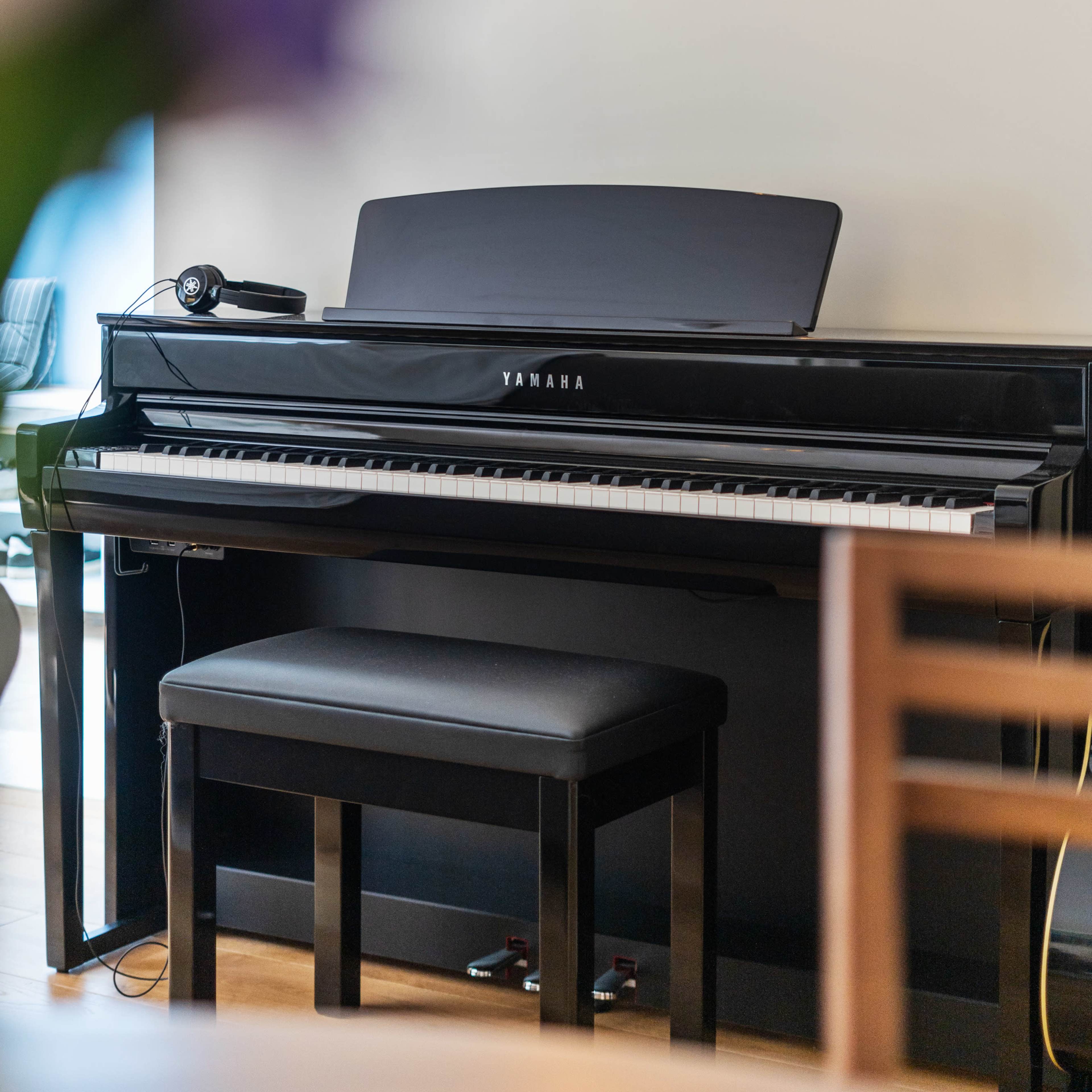 A black Yamaha piano is positioned against a light-colored wall with a single hanging light fixture above it.