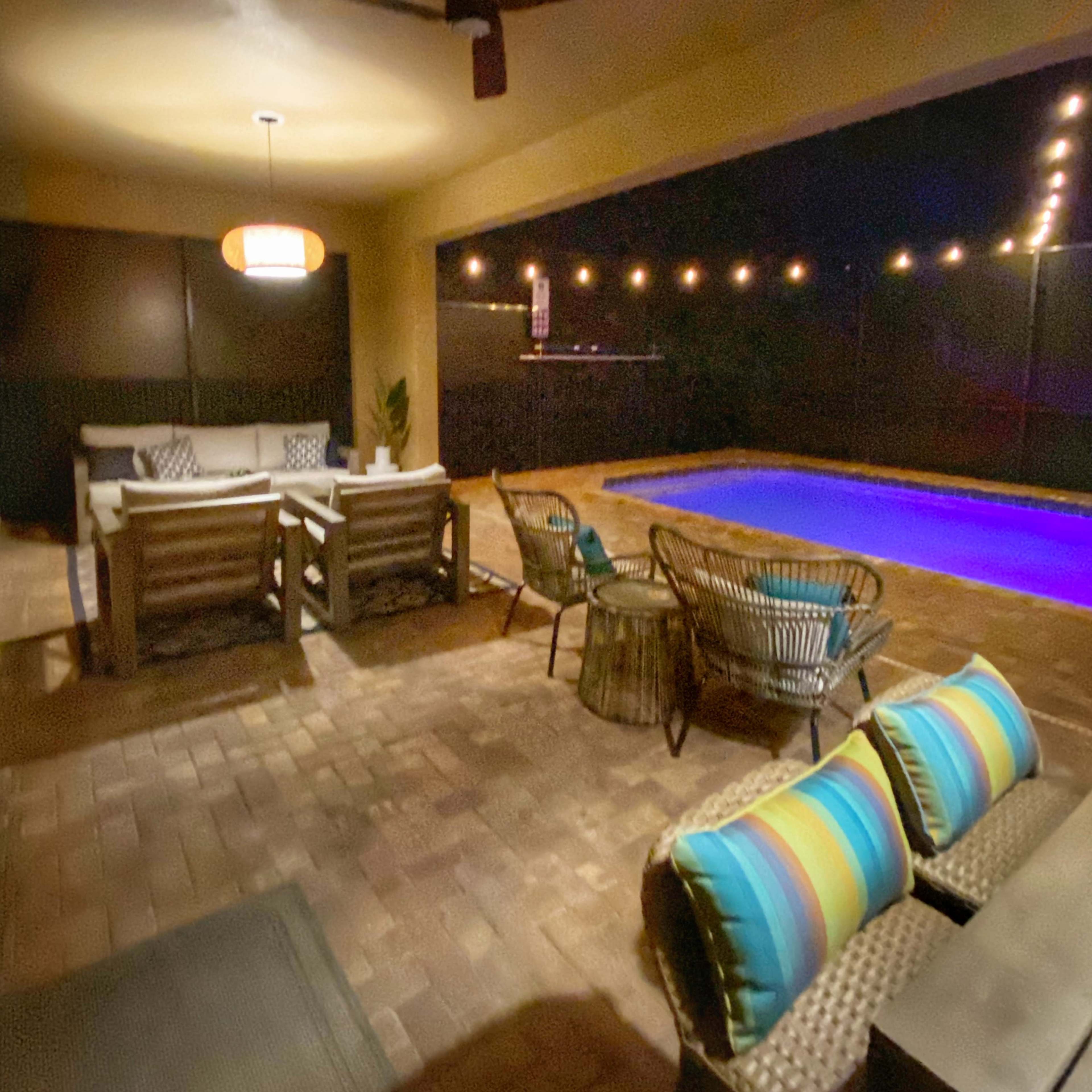 A nighttime outdoor patio featuring seating arrangements and a swimming pool illuminated with blue lights.
