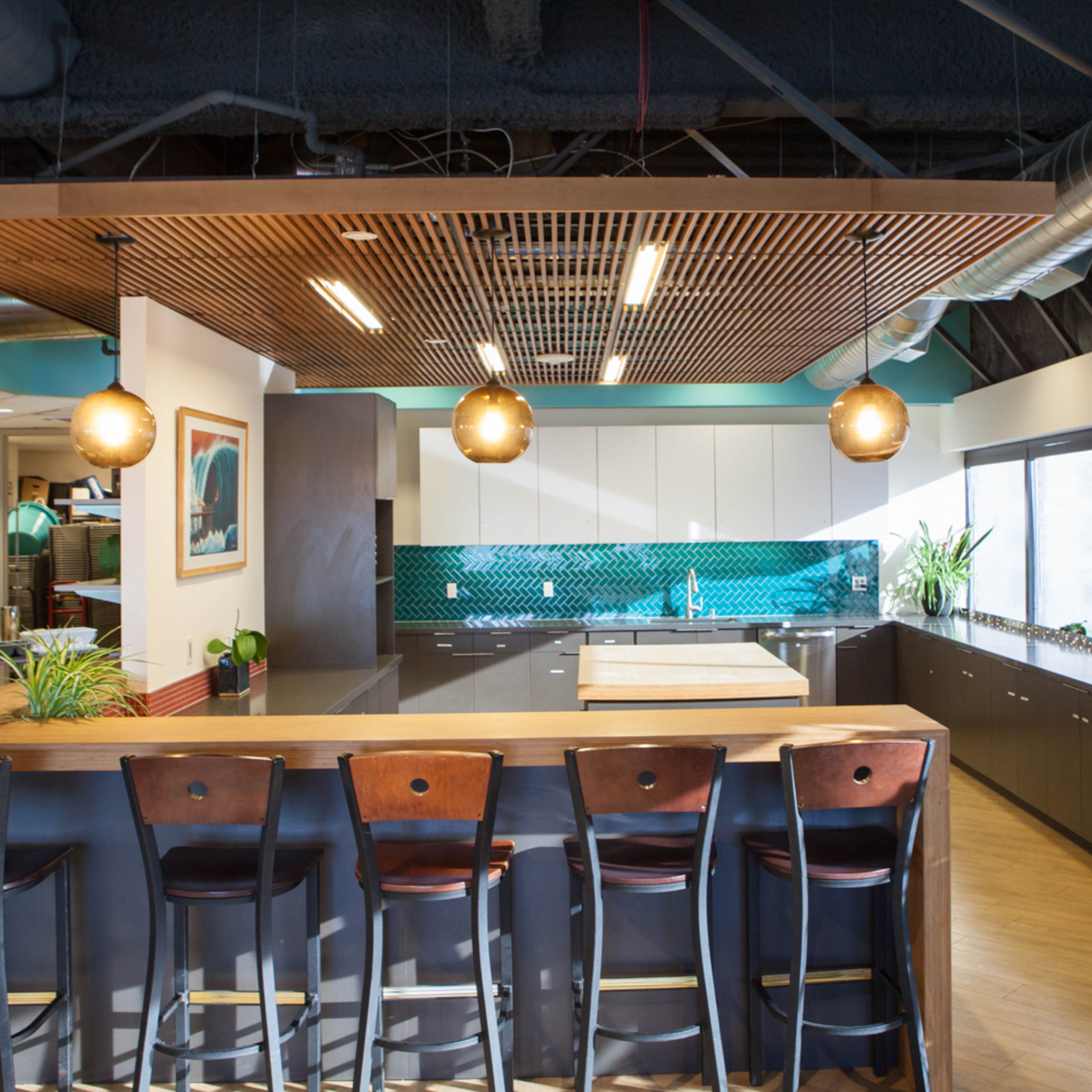 A modern kitchen with a long island counter, bar stools, and large windows that let in natural light.