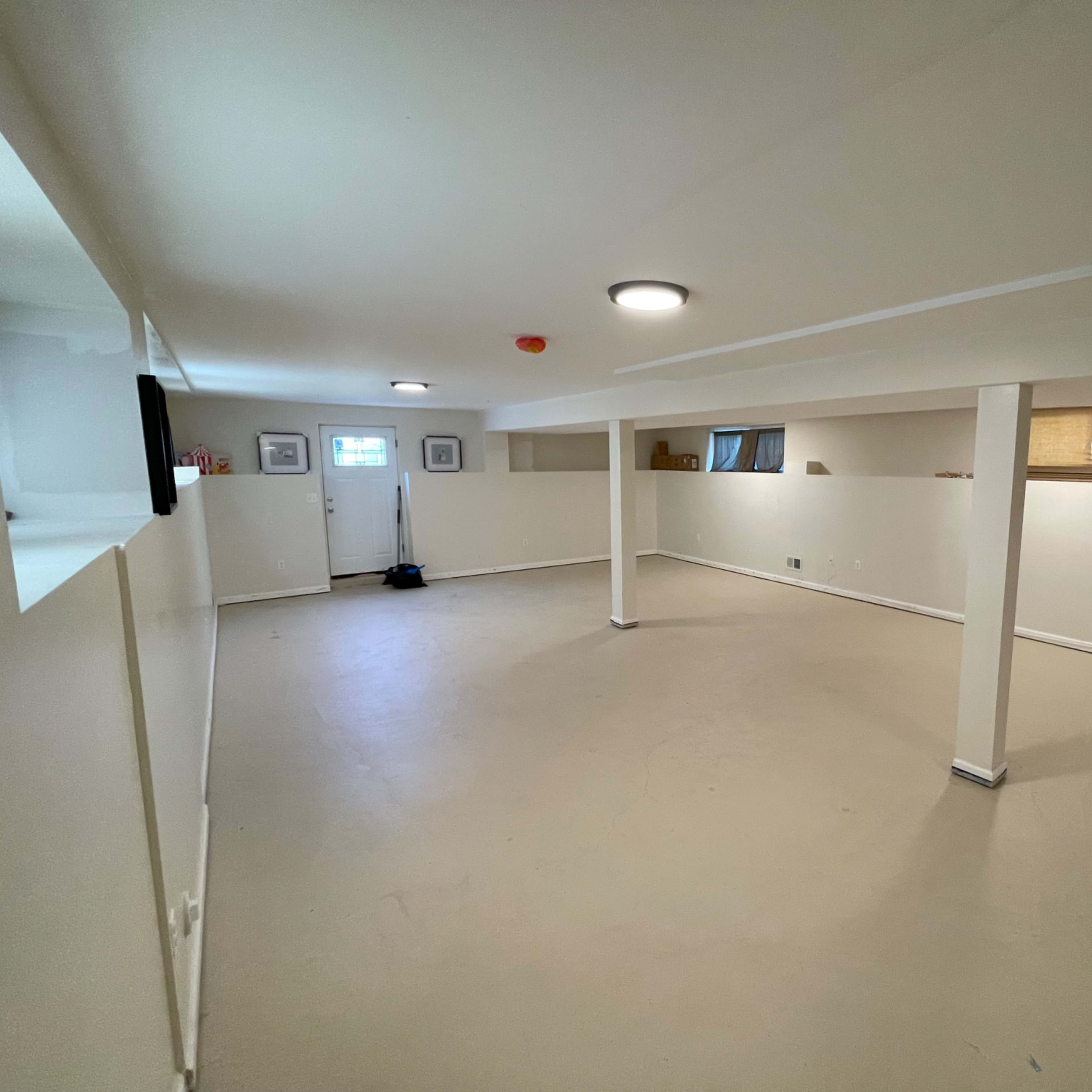 A spacious, empty basement with light-colored walls and a concrete floor, featuring windows and a door.