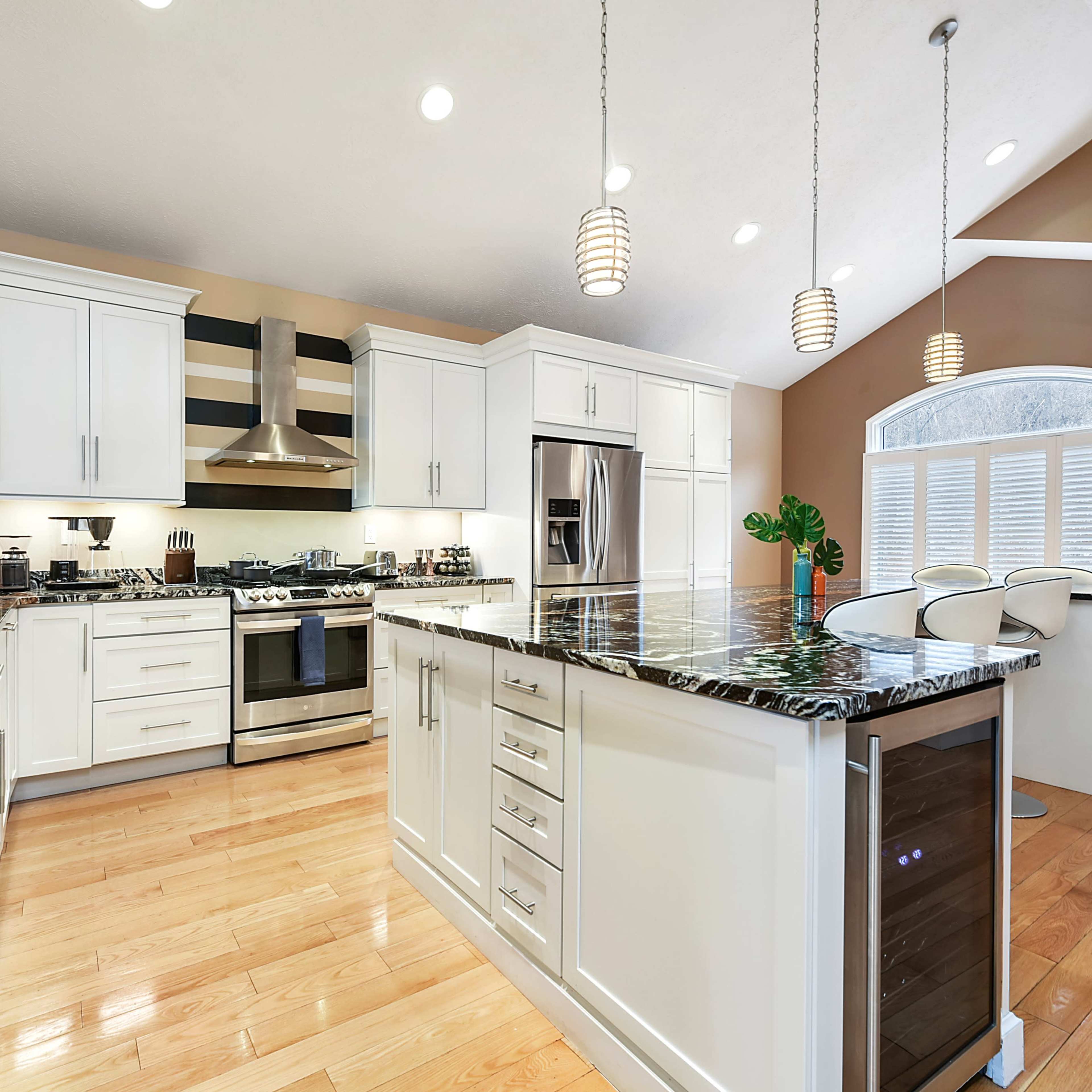 A modern kitchen features white cabinetry, a large island with dark granite countertops, stainless steel appliances, and pendant lighting.