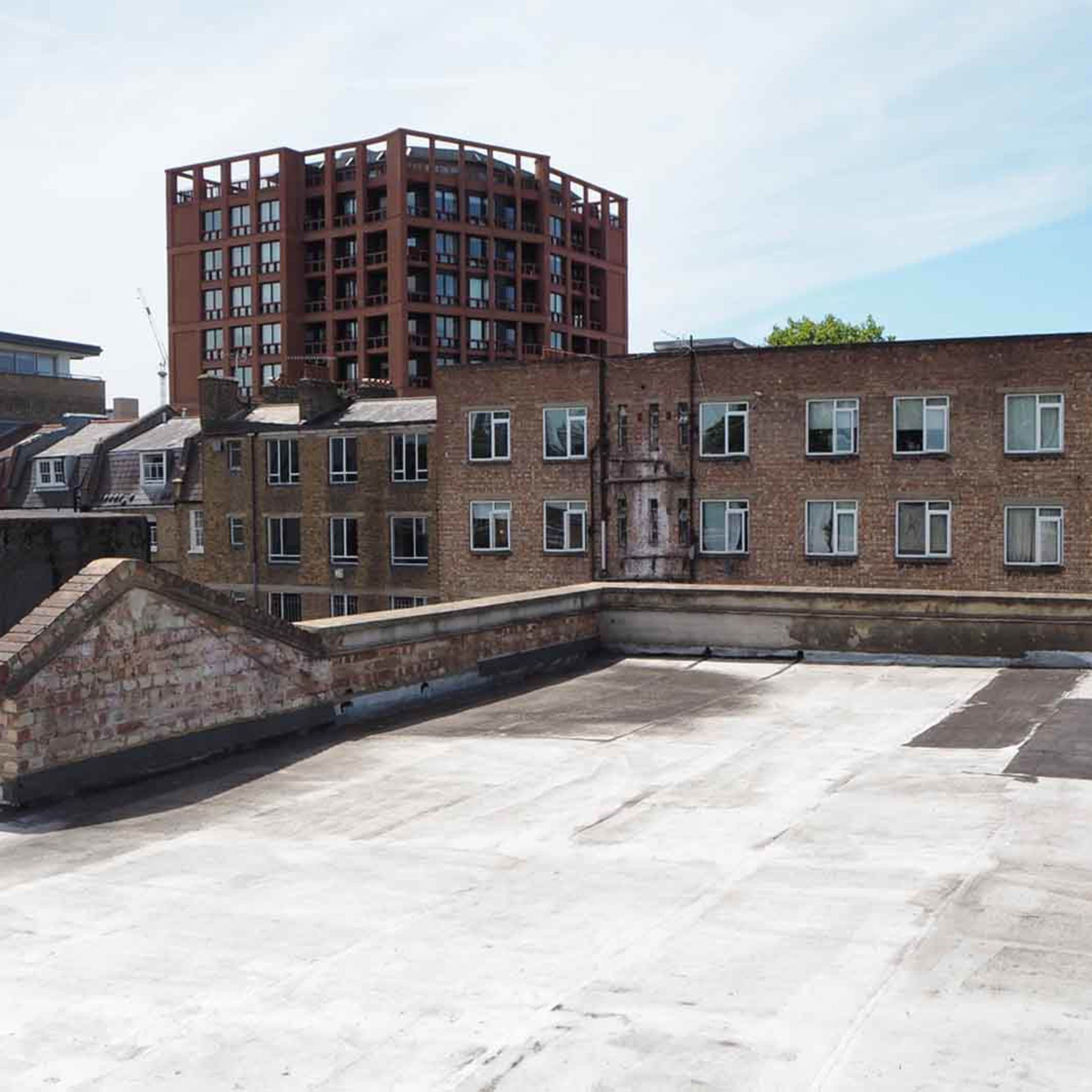 A flat rooftop with several buildings in the background, including a brick structure and a taller red building.
