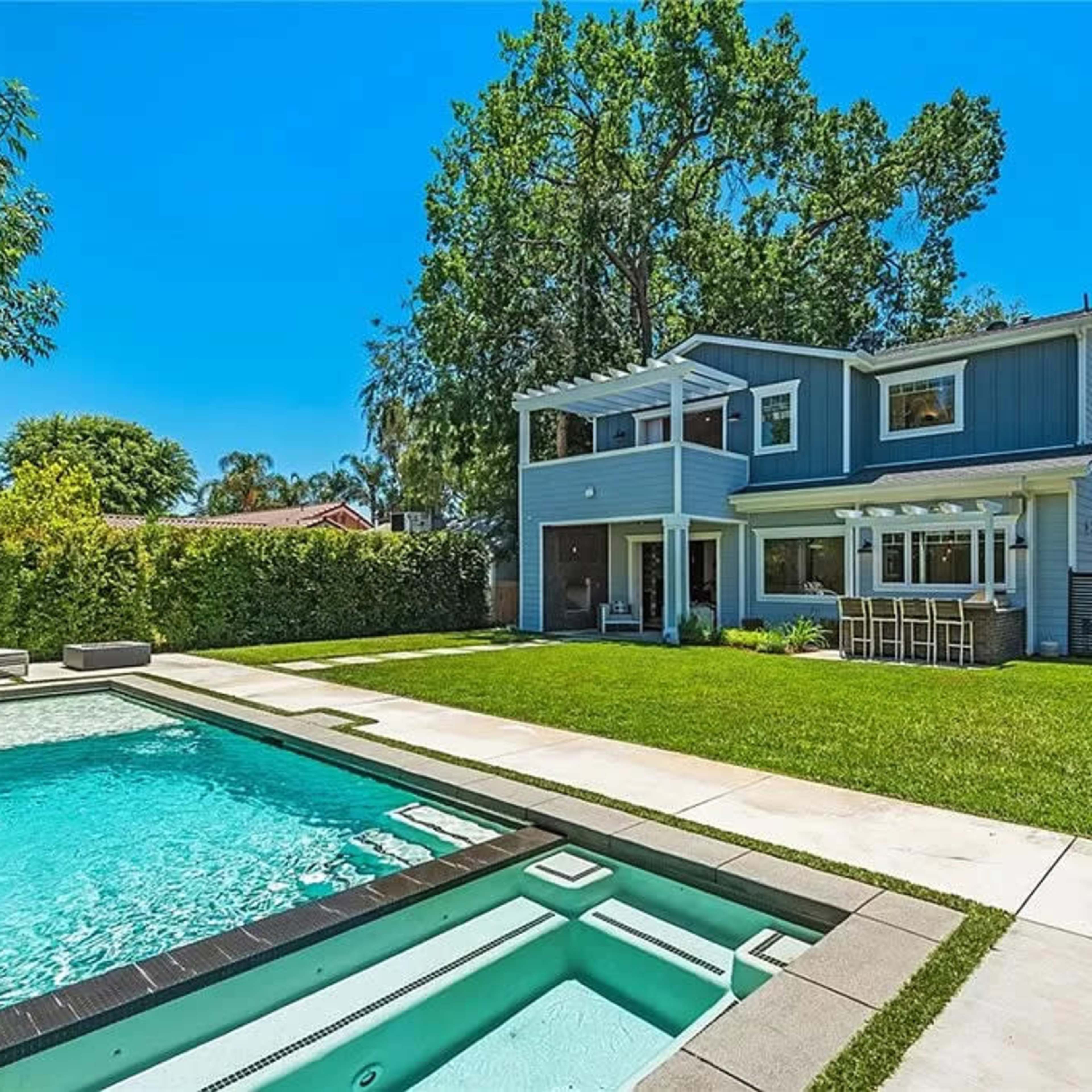 A modern two-story house with a swimming pool and spa surrounded by a well-maintained lawn and landscaping.