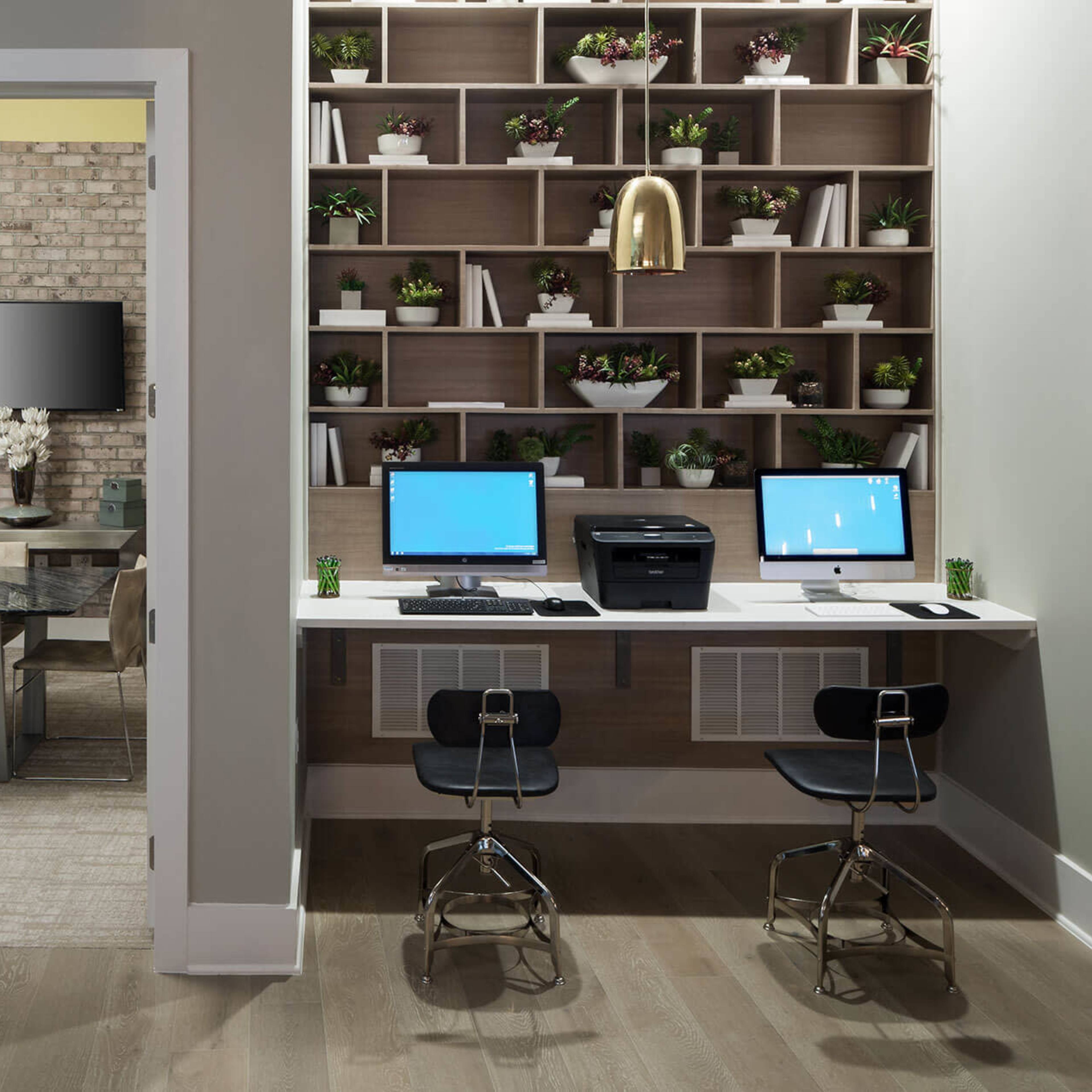 A modern office space featuring a conference room with a large table and a separate work area with two computers and a printer against a wall of shelves filled with plants.