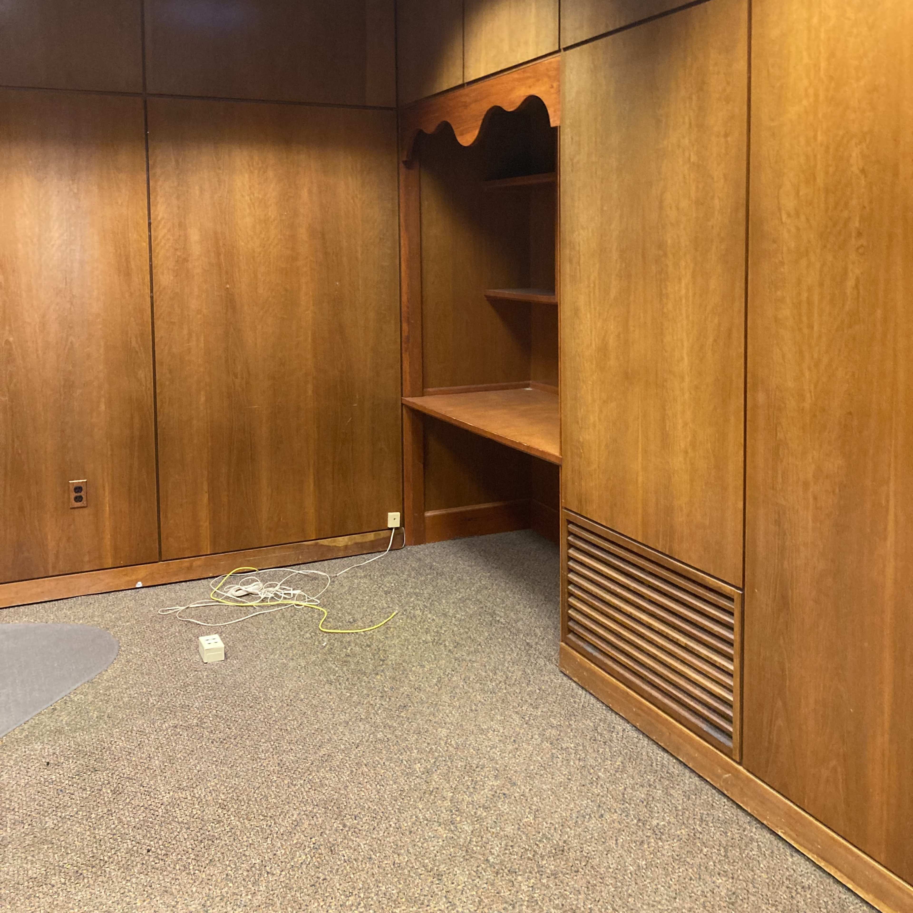 A spacious room with wooden paneling, featuring a built-in shelf and a carpeted floor.