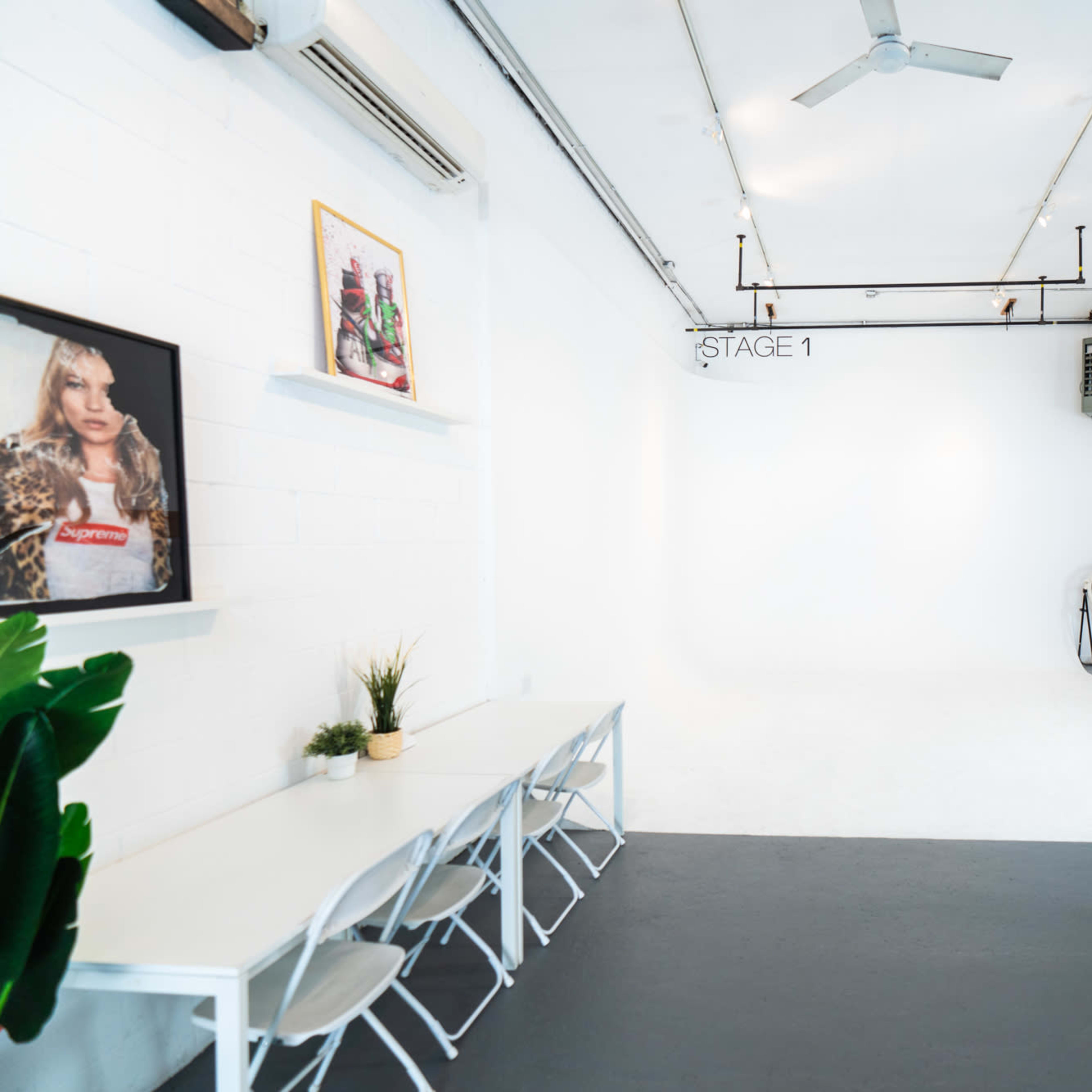 A spacious, well-lit studio with a white backdrop, a fan, a wooden counter, and a table with chairs.