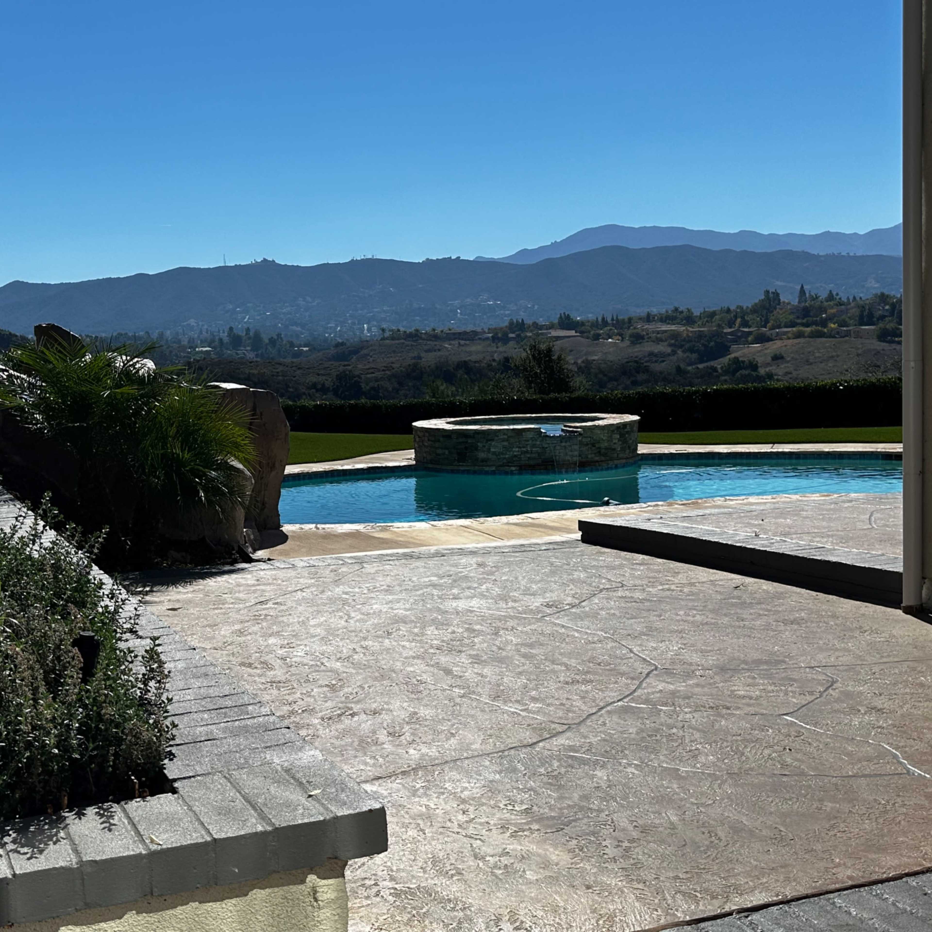 A clear view of a swimming pool surrounded by landscaped greenery and mountains in the background.