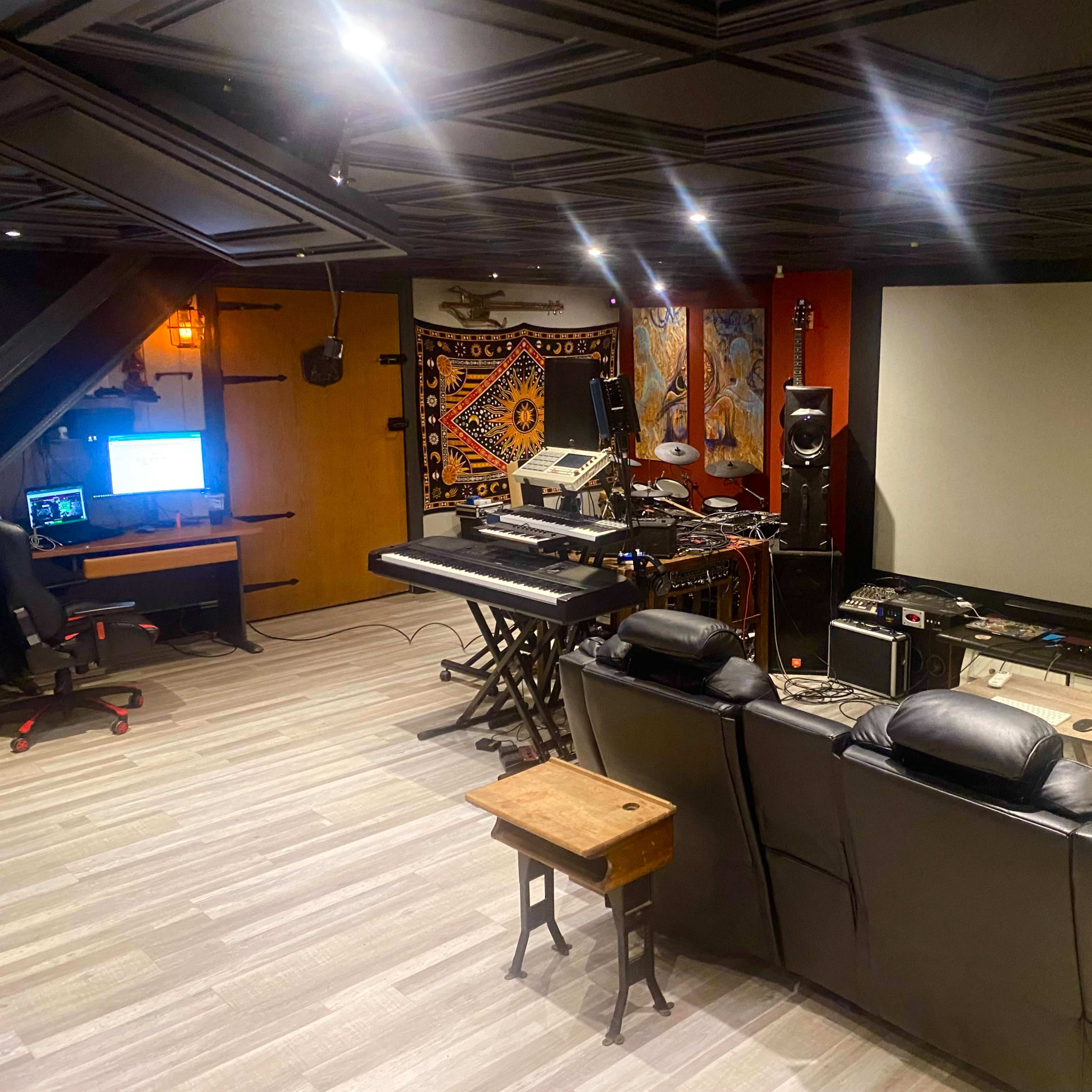 A home theater and music production studio featuring a large screen, a keyboard setup, and seating in a dimly lit room.