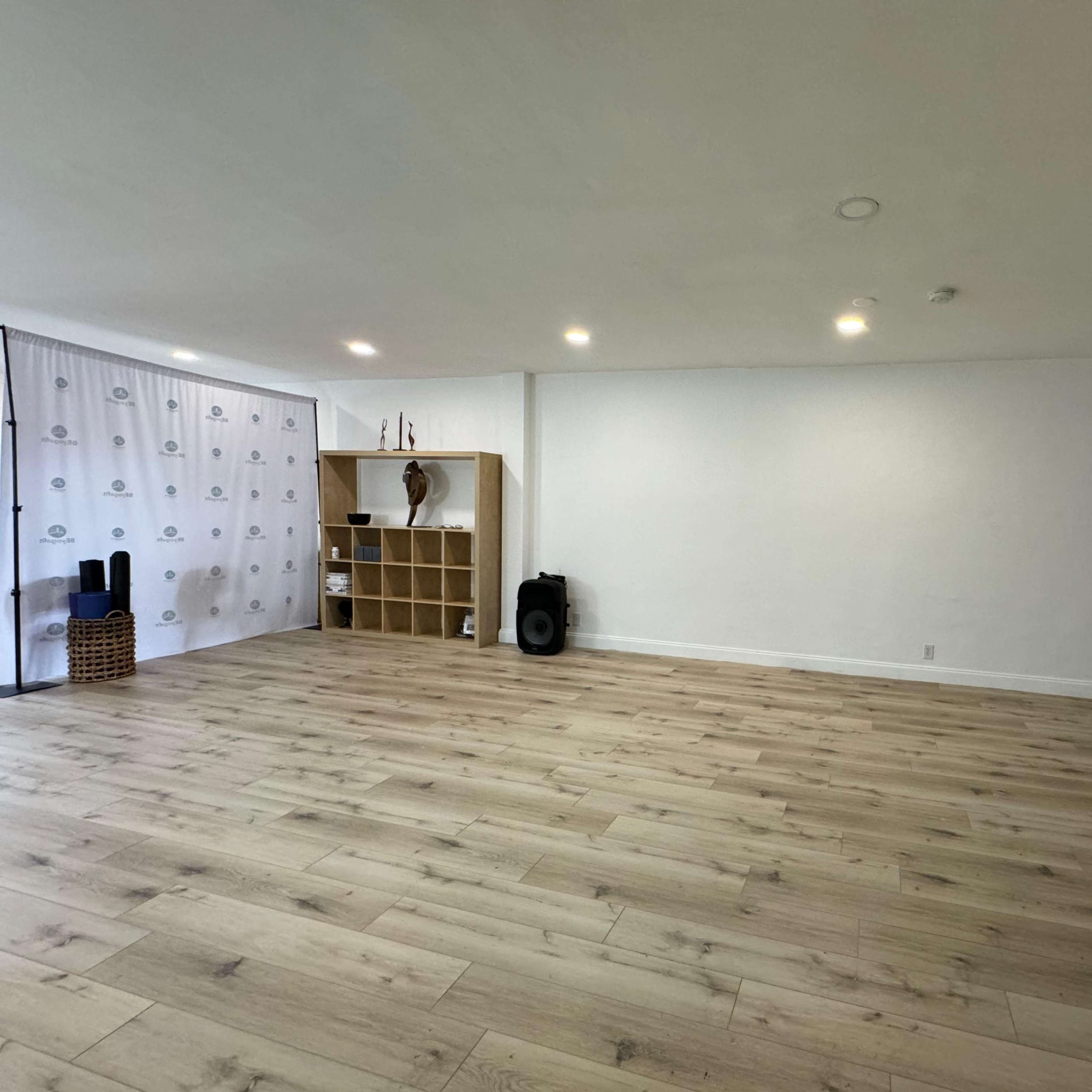 A spacious room with light wooden flooring, a simple bookshelf, and a backdrop featuring a patterned curtain.