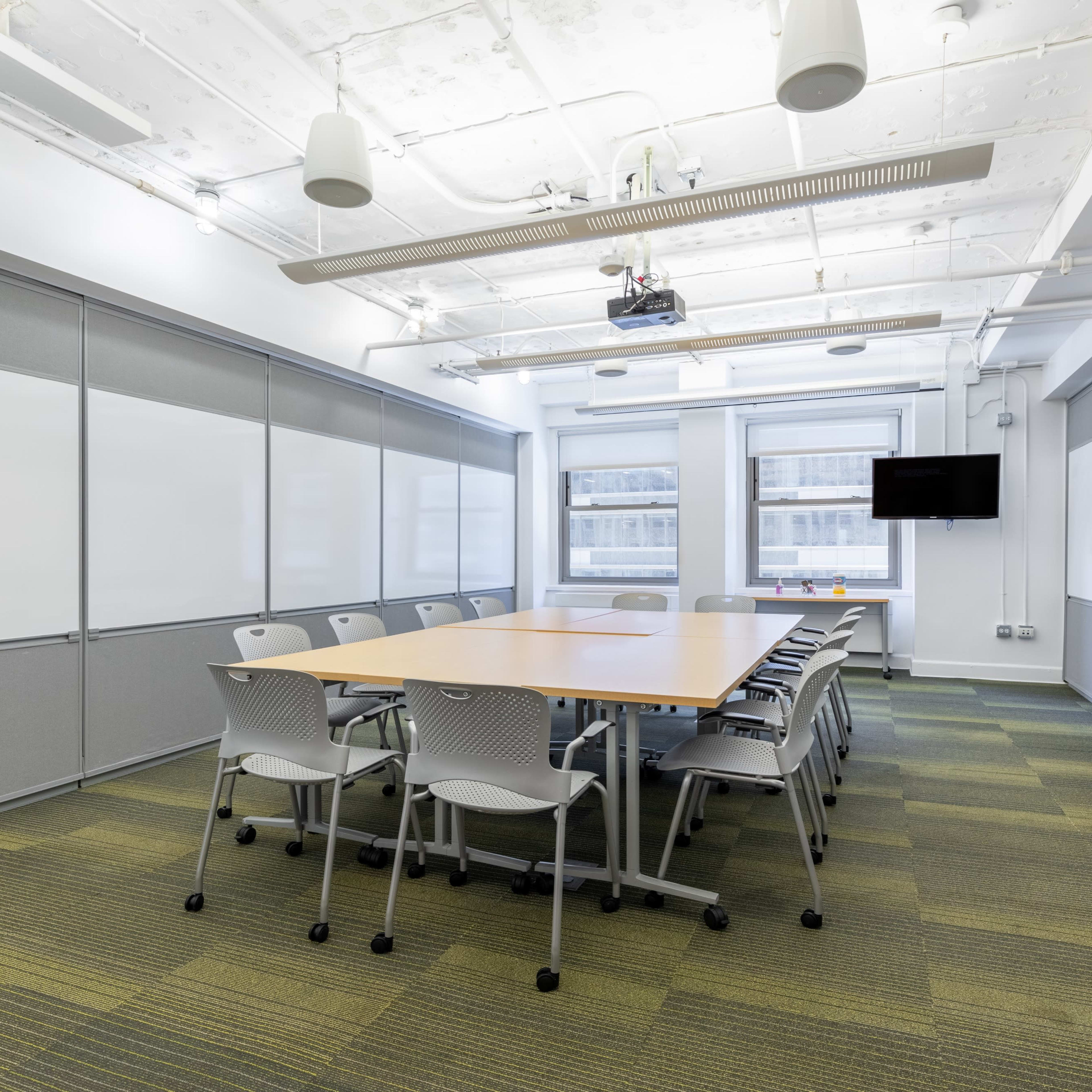 A conference room with a large table surrounded by chairs, whiteboards on the walls, and a projector and screen at one end.