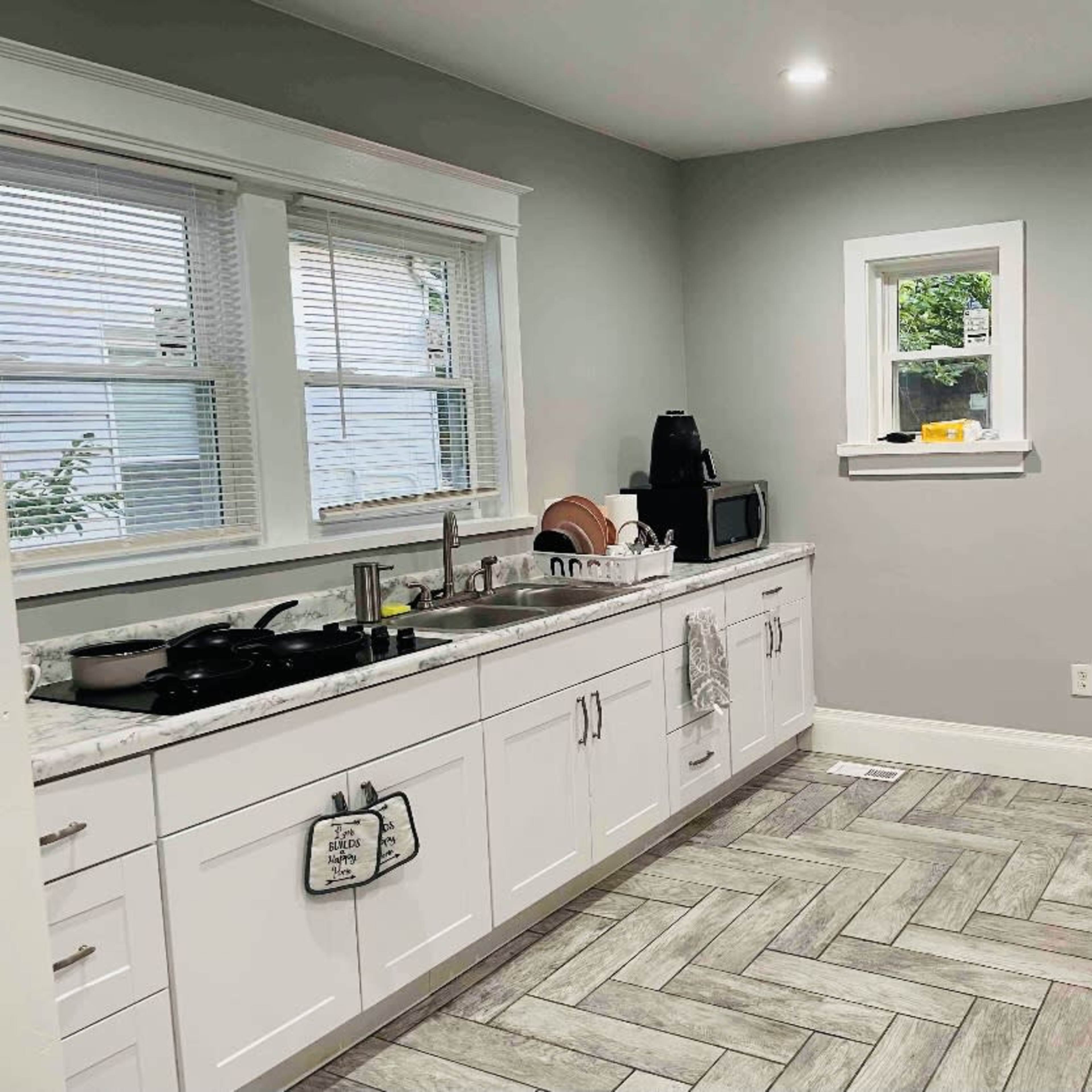 The kitchen features white cabinetry, a large stainless steel refrigerator, and a light gray color scheme with a herringbone patterned floor.