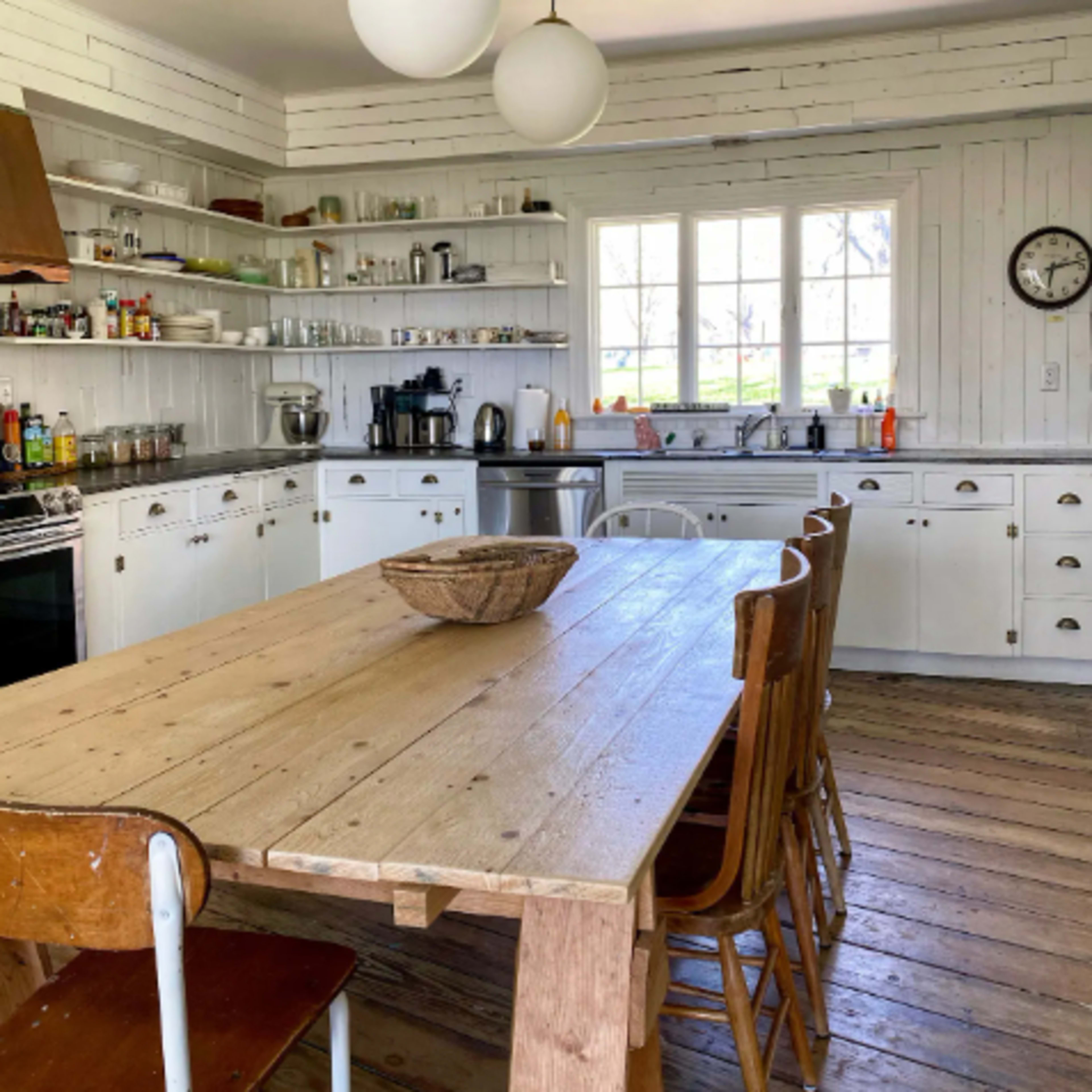 A spacious kitchen features white cabinetry and shelves filled with jars and utensils, along with a wooden table and six chairs.