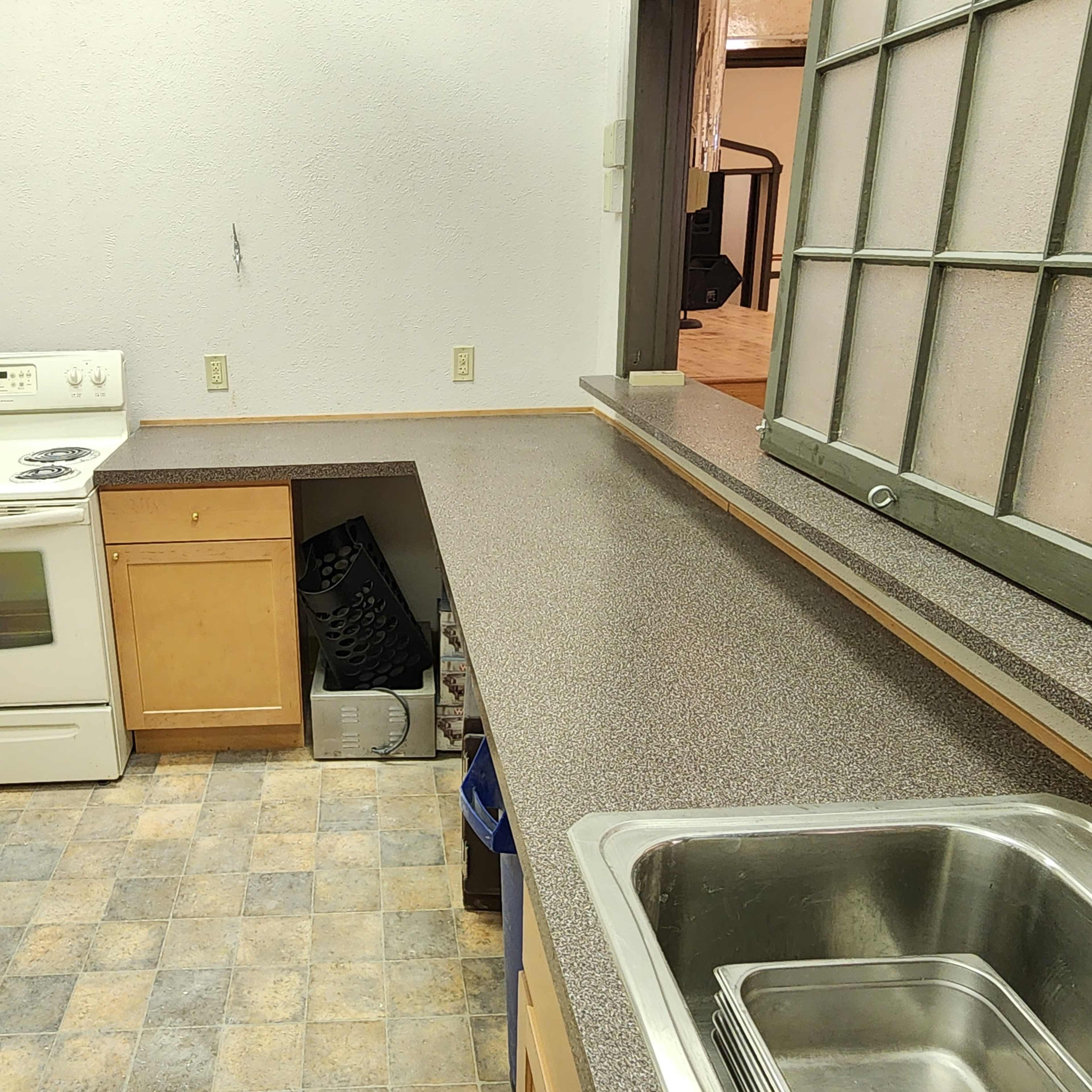 A kitchen with a stove, sink, and a countertop, featuring light-colored cabinets and a patterned floor.