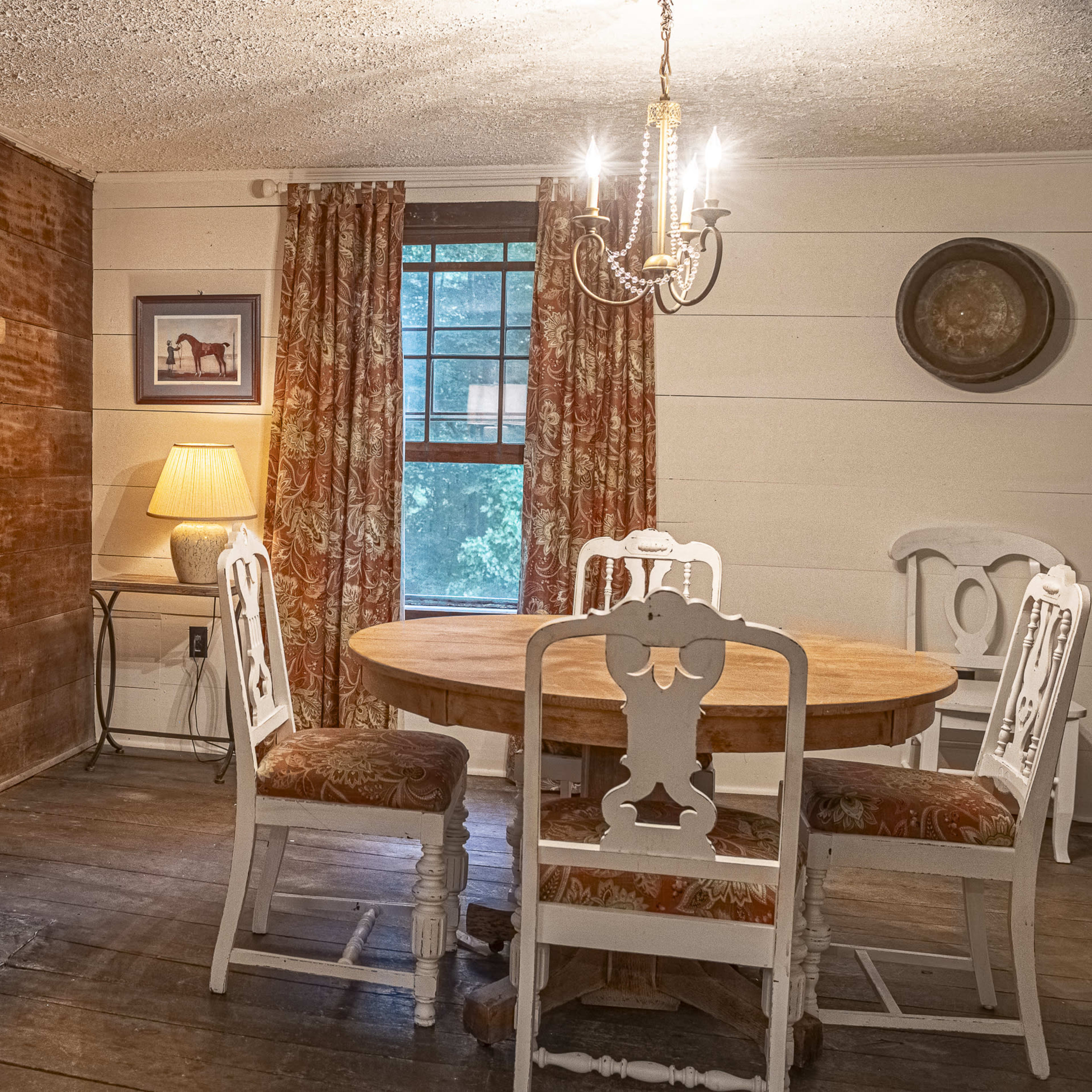 A cozy dining area featuring a round wooden table surrounded by four white chairs, a stone fireplace, and a light fixture hanging overhead.