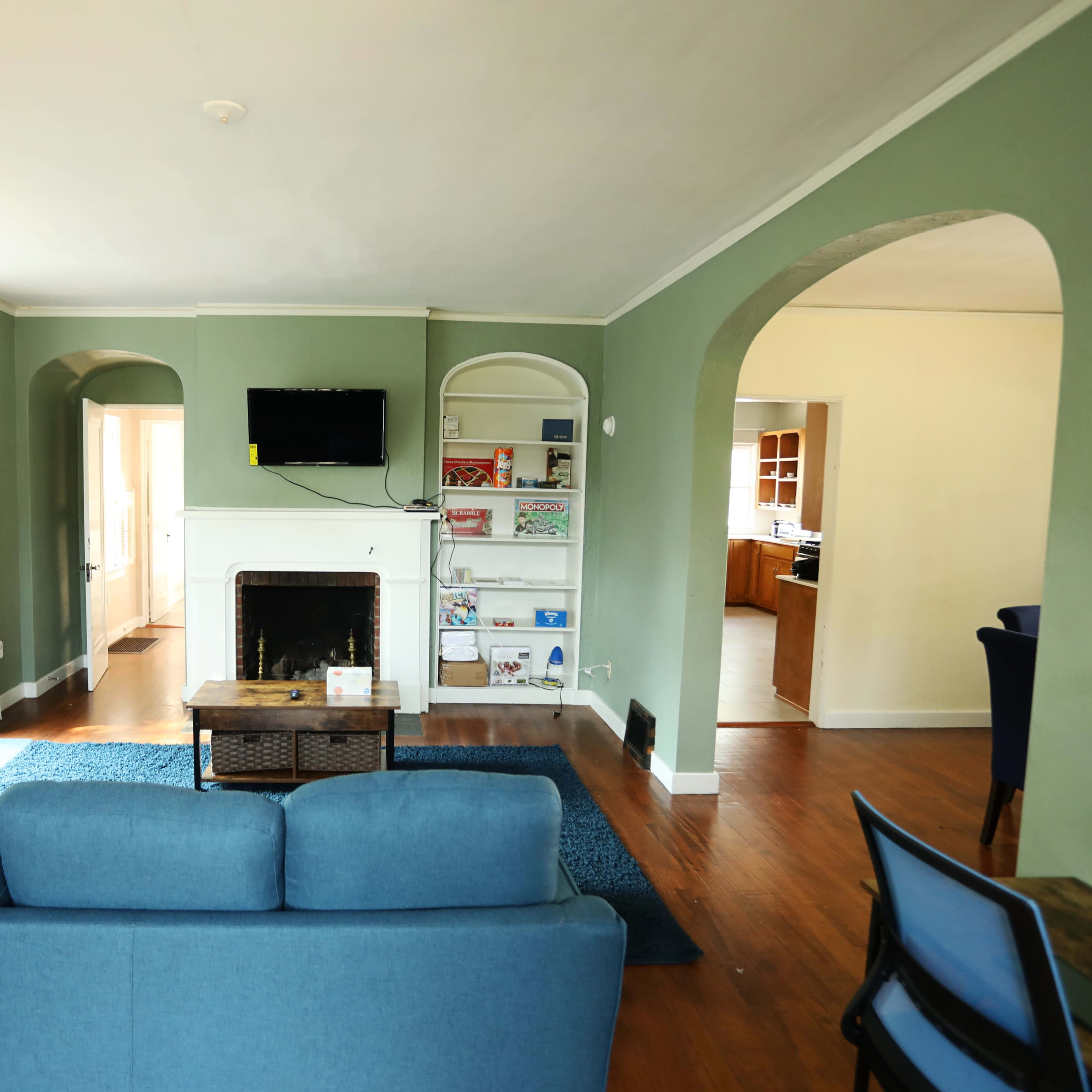 A living room with green walls, a blue sofa, a fireplace, and arched doorways leading to a kitchen area.