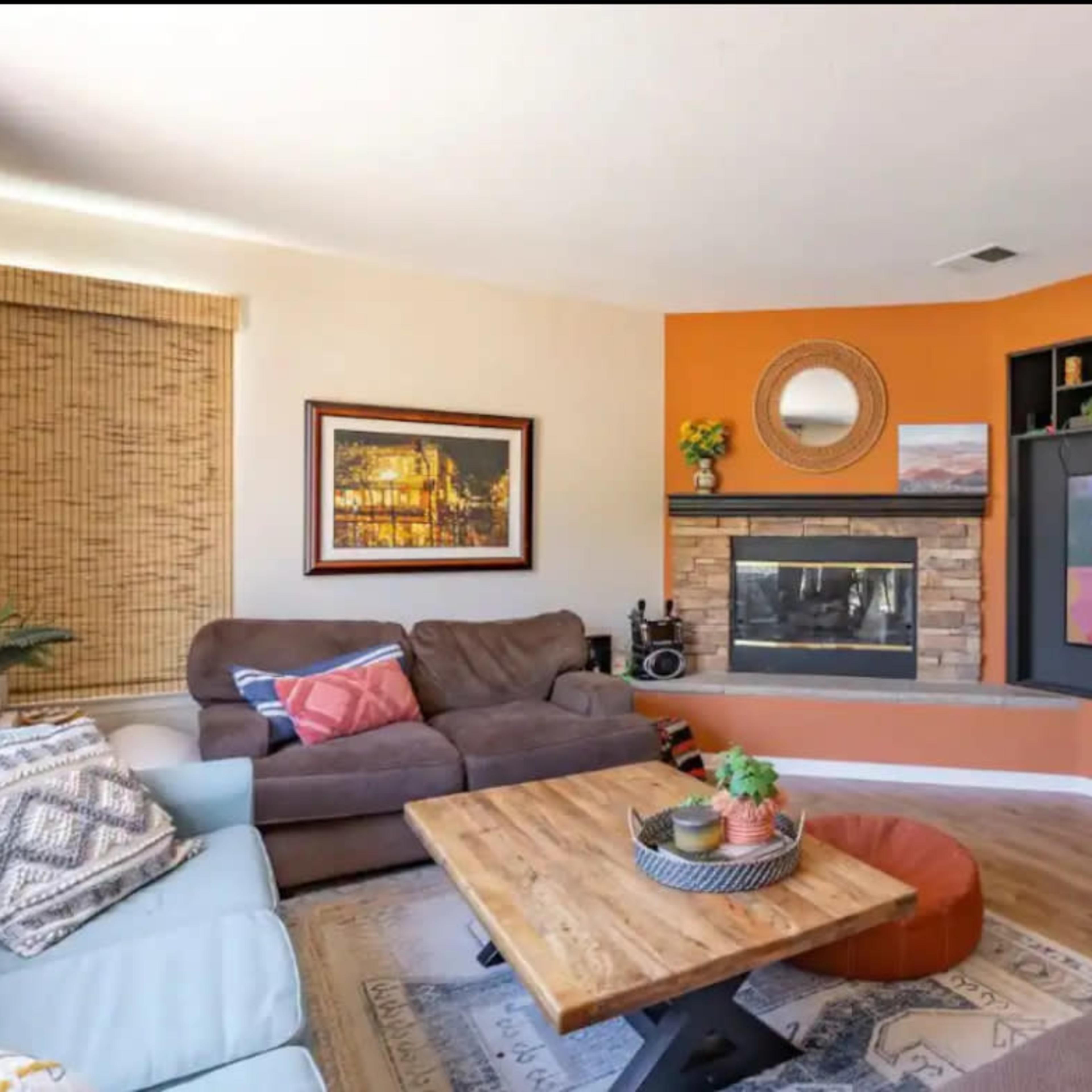 A living room with a brown sofa, a light blue couch, a wooden coffee table, and a fireplace surrounded by orange and neutral walls.