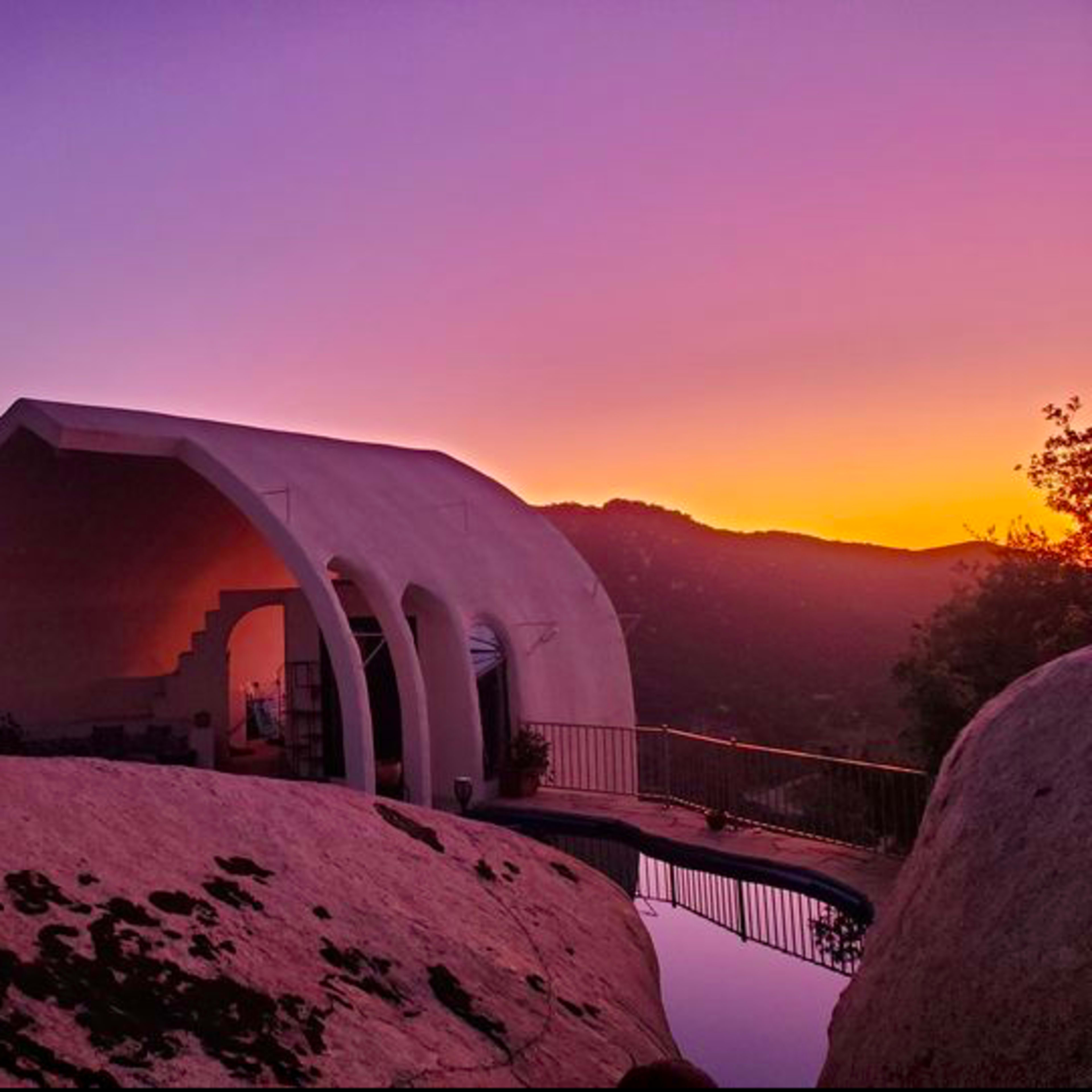 A unique architectural structure sits on rocky terrain, overlooking a colorful sunset.