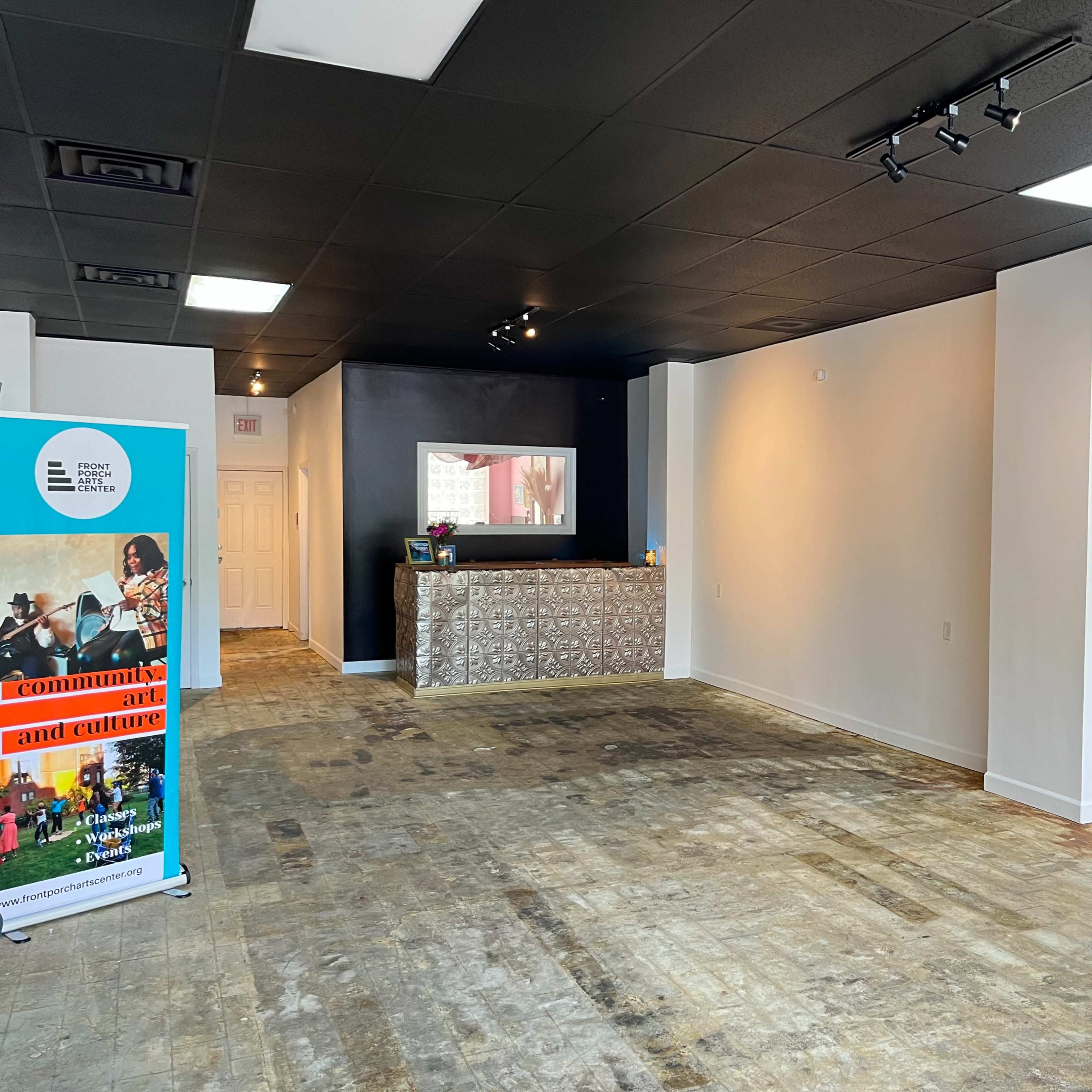 An empty room with a light-colored wall, a dark reception area with a countertop, and a display sign on the left side.