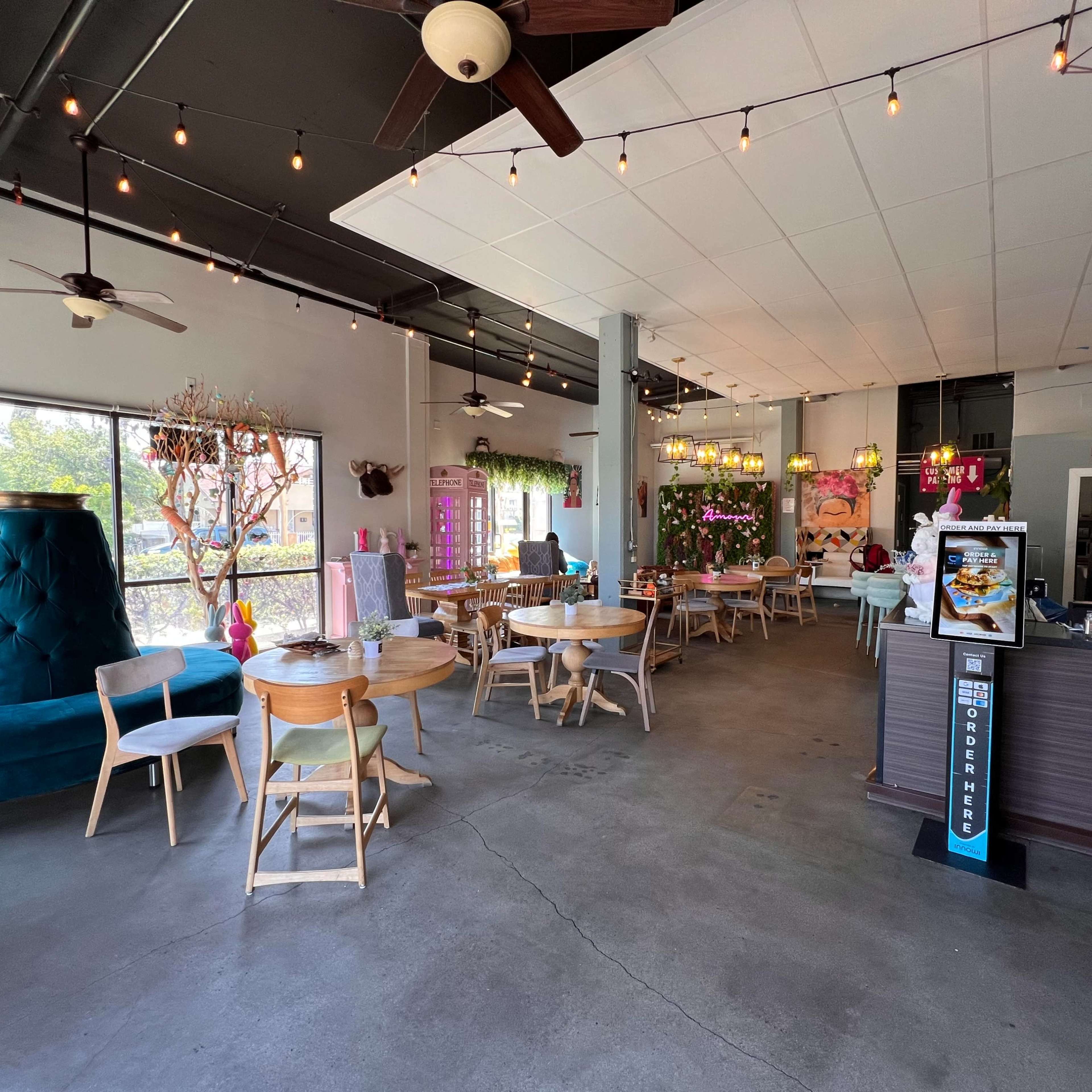 A spacious café with wooden tables and chairs, large windows, and decorative plants.