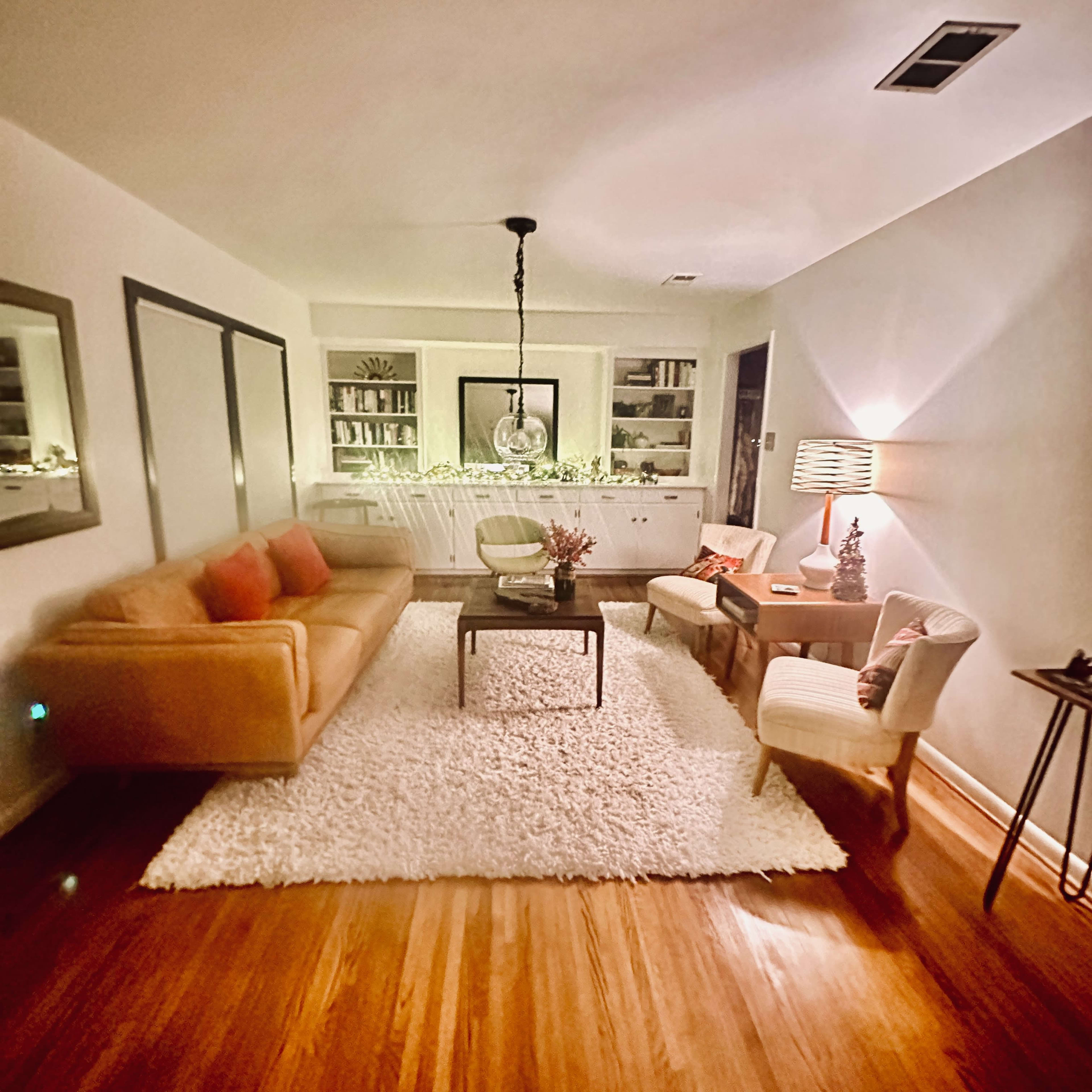 A cozy living room with a sofa, two chairs, a coffee table, and bookshelves against the walls, all on a plush white rug.