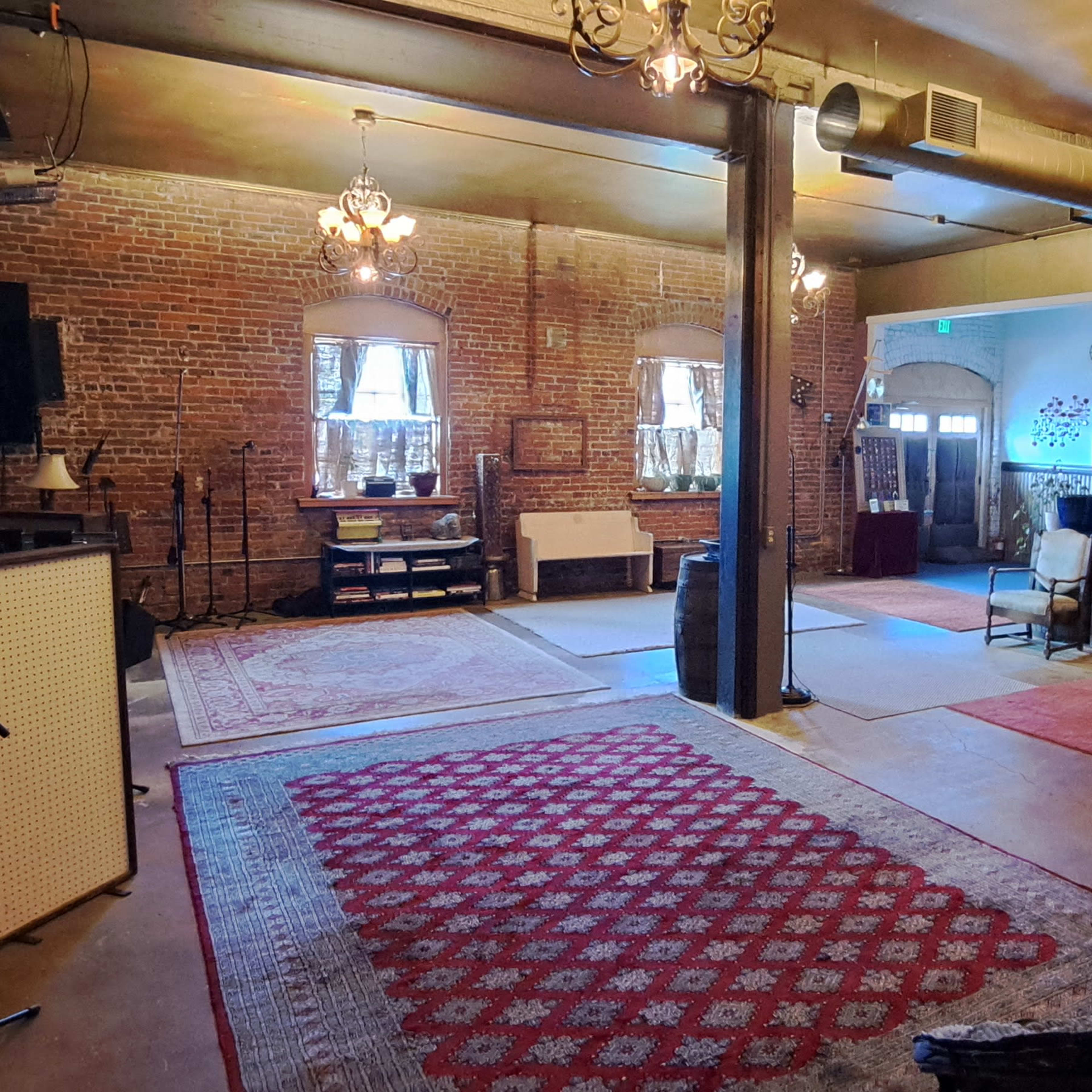 An interior space with exposed brick walls, a mix of seating arrangements, and various lighting fixtures hanging from the ceiling.