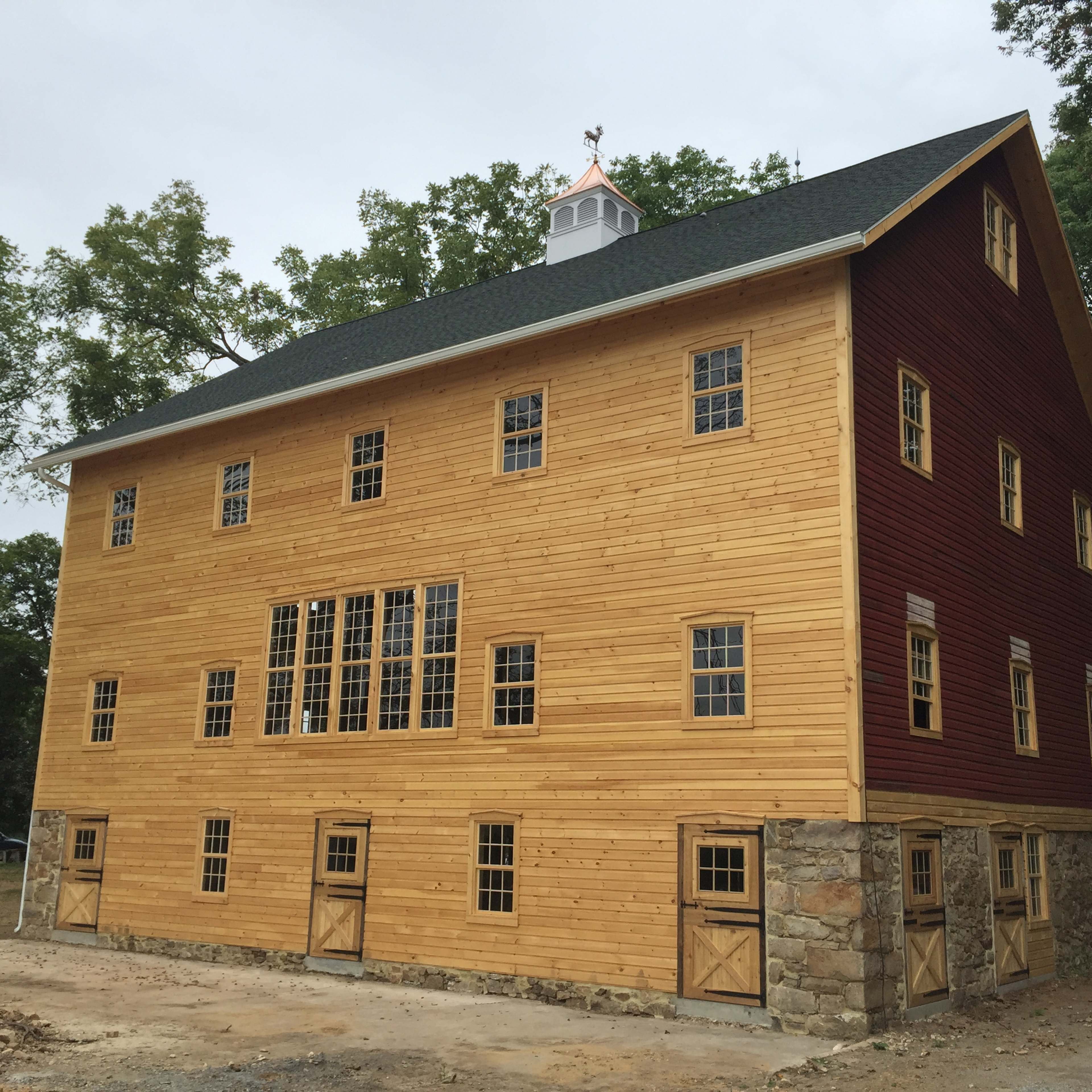 A large, two-tone wooden barn with a stone foundation and multiple windows on its side.