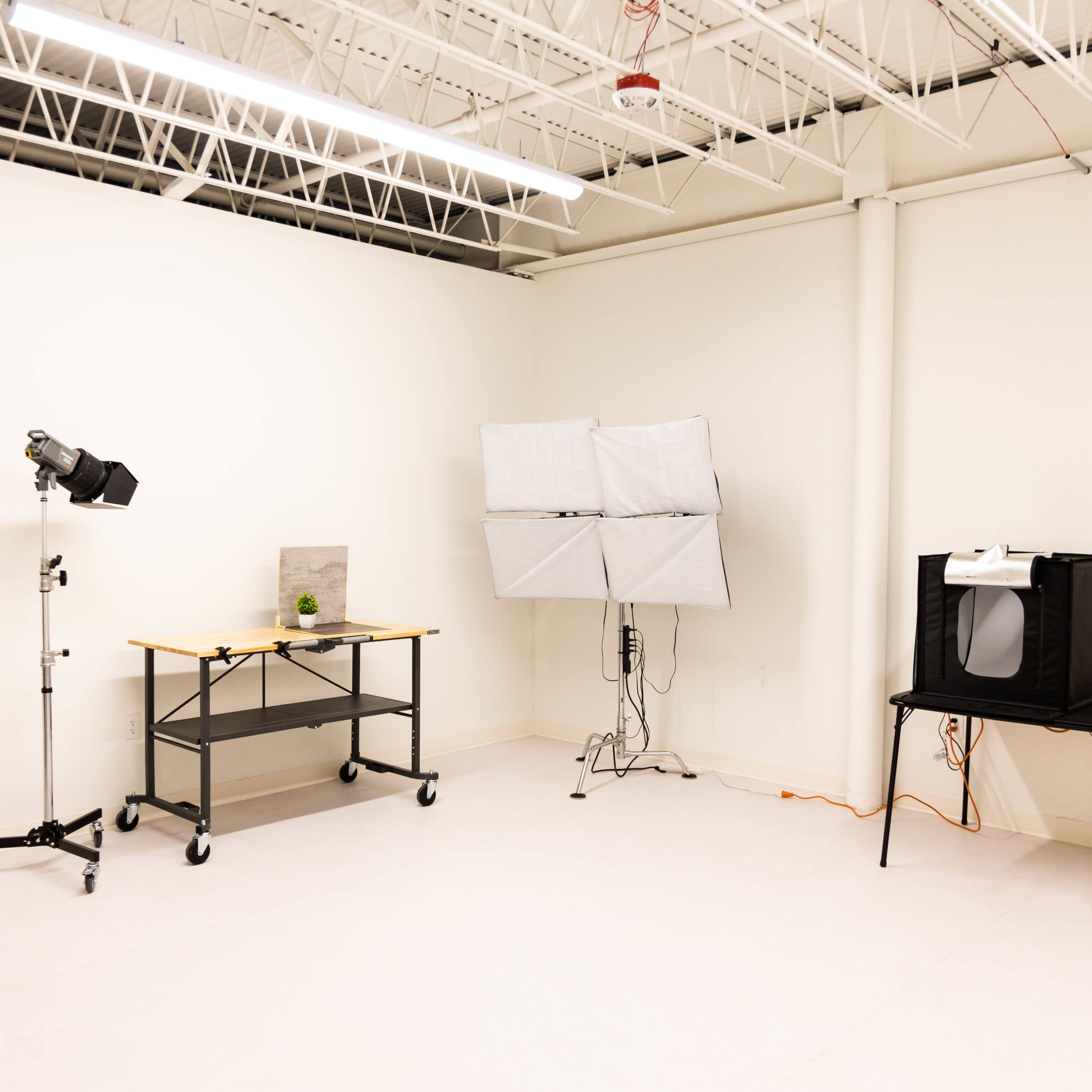 A minimalist photography studio with a table, softbox lighting, and a backdrop setup against a plain white wall.