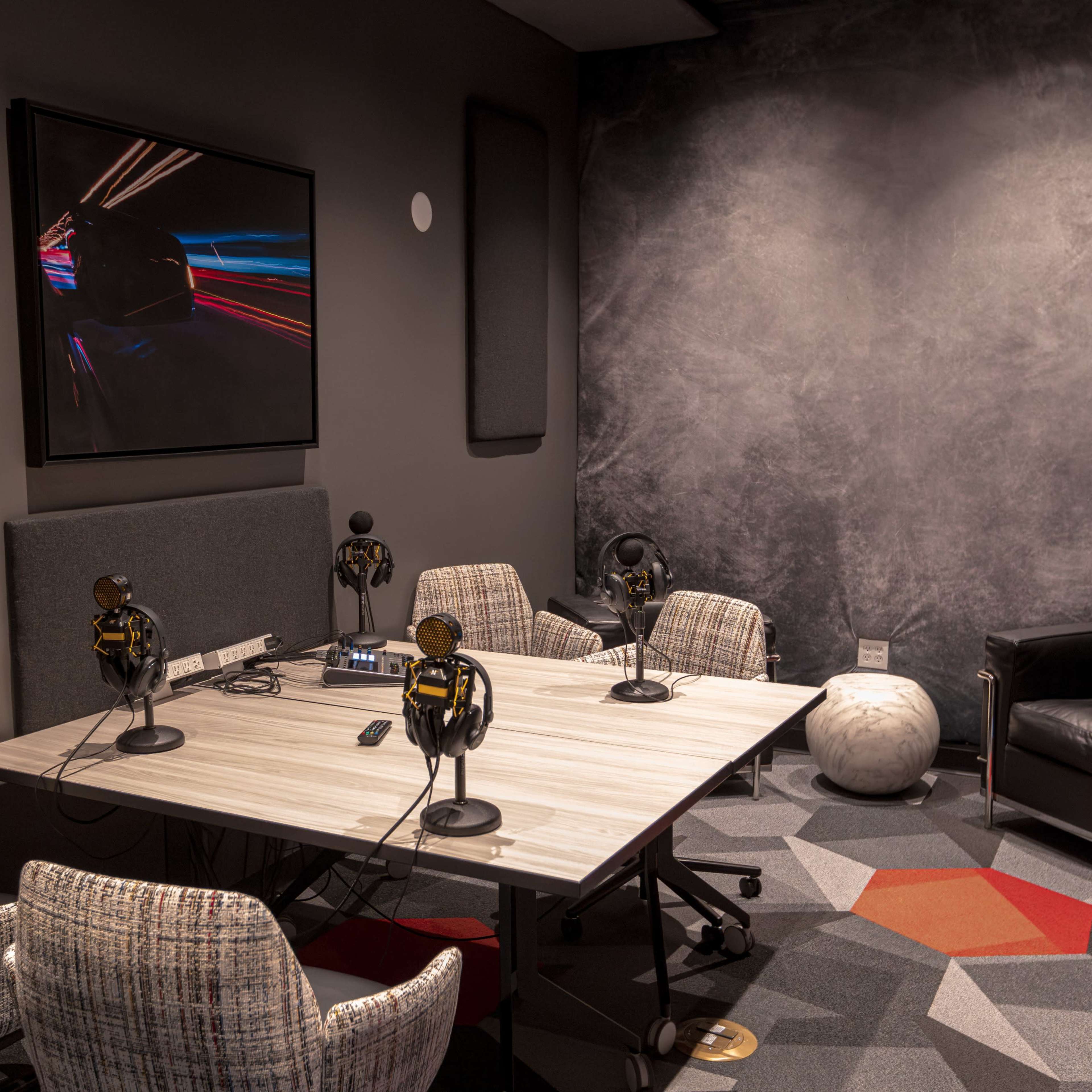 A modern recording studio with a table, four chairs, microphones, and sound equipment against a textured gray wall.