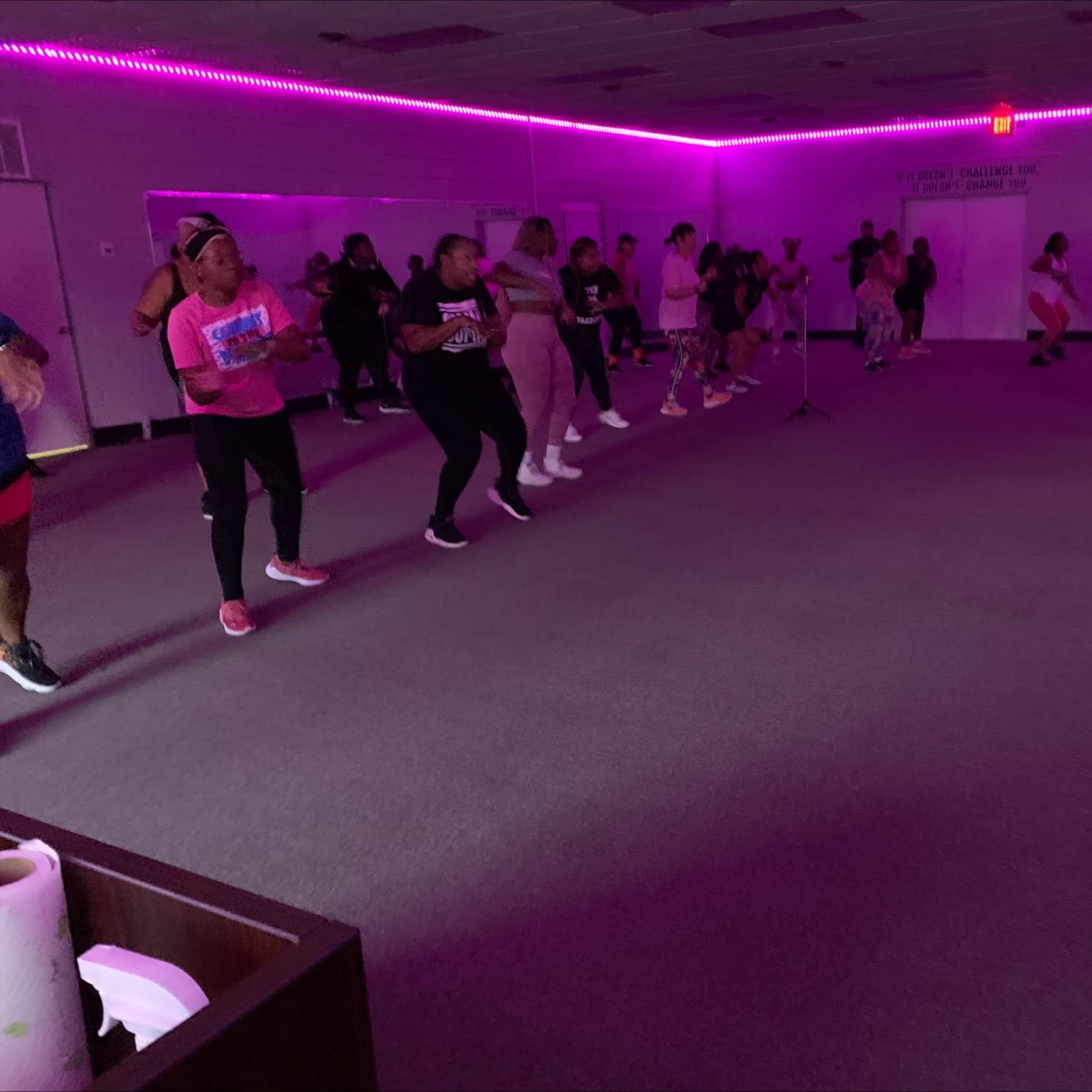 A group of people are participating in an exercise class in a room lit with purple lights.