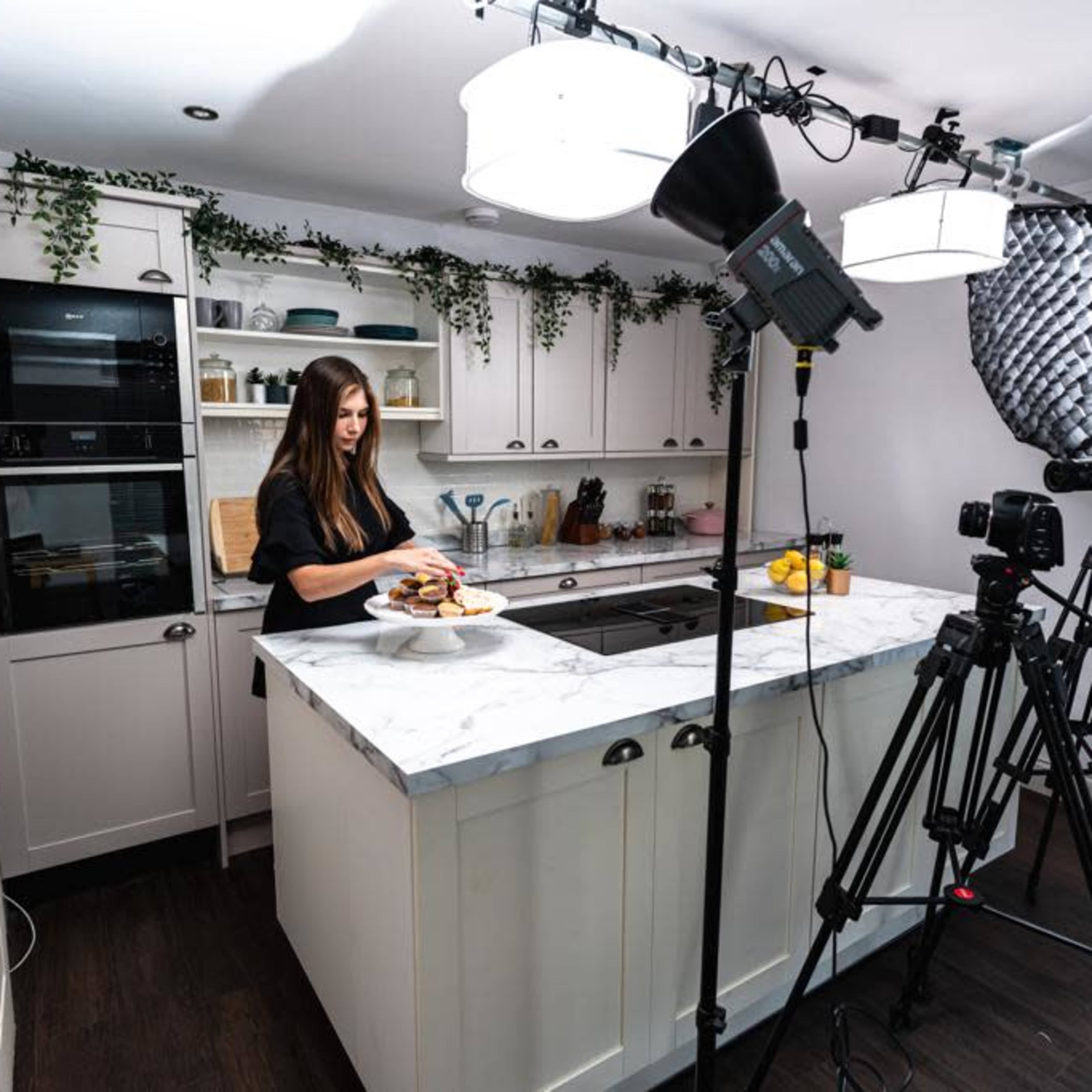 A woman is preparing a dish on a marble countertop in a well-lit kitchen equipped for filming.