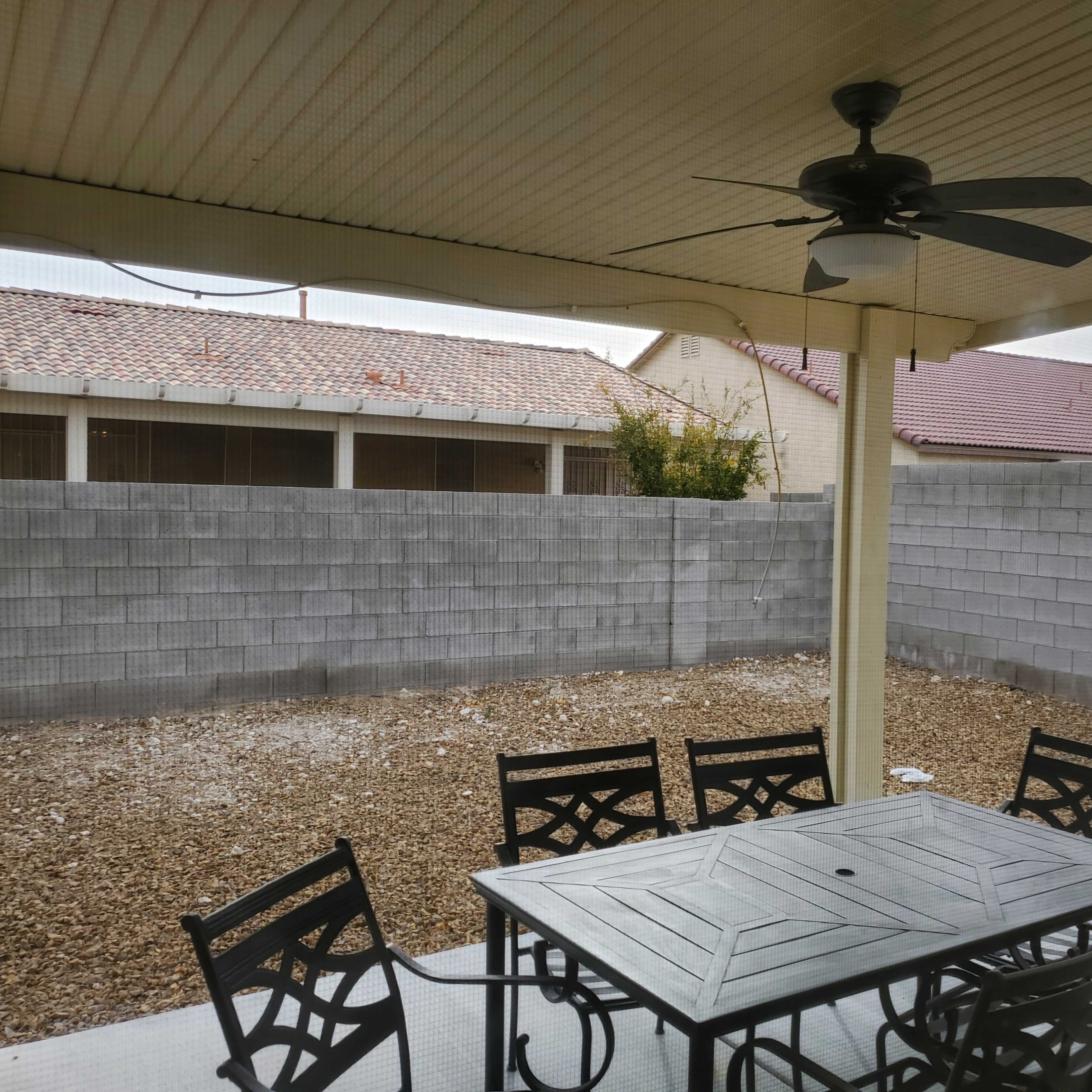 A patio area with a table and chairs overlooks a gravel yard surrounded by a gray concrete wall.