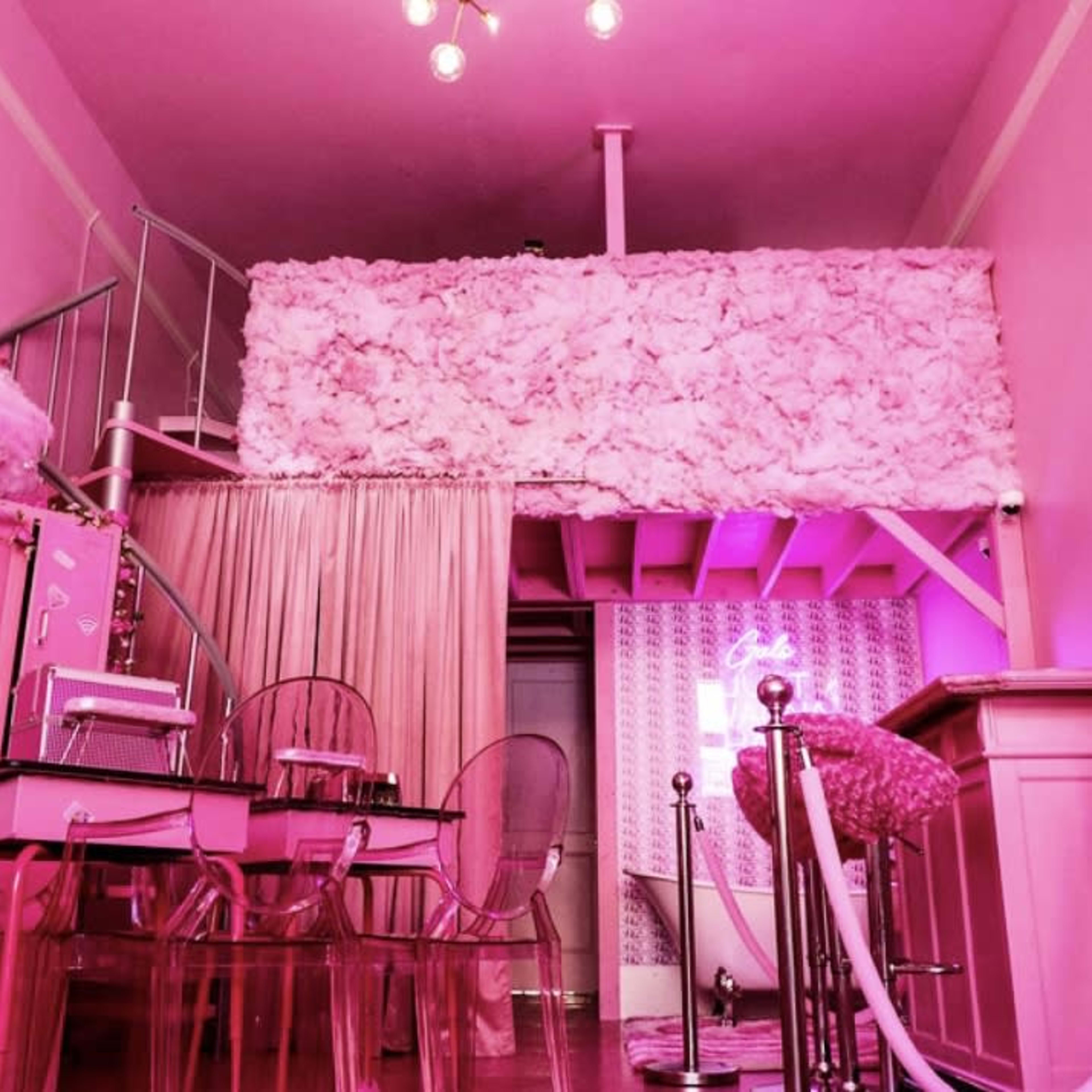 A vibrant, pink-themed café interior with floral decor, transparent chairs, and neon signage.