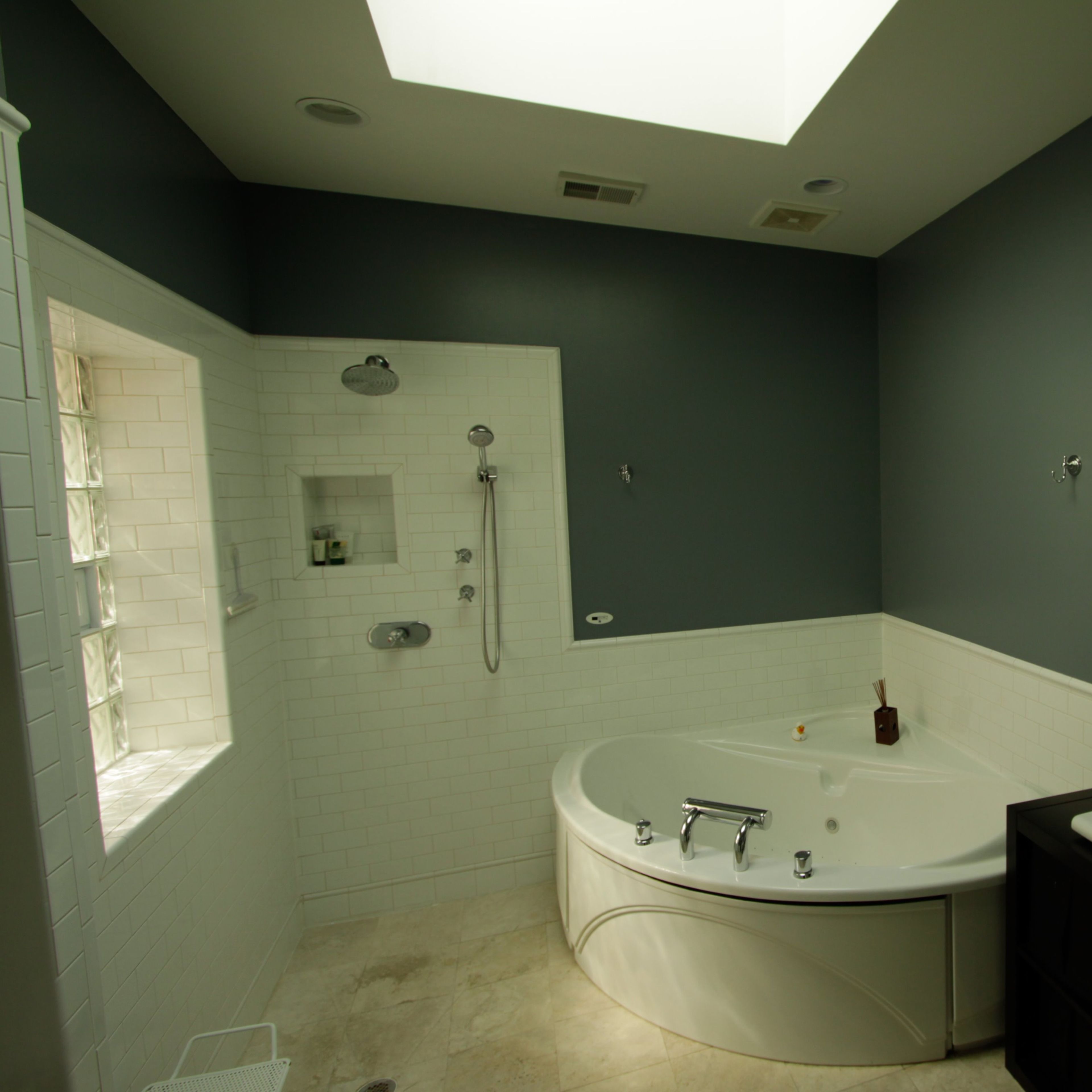 A modern bathroom featuring a corner bathtub, a walk-in shower, a double sink vanity, and a large skylight.