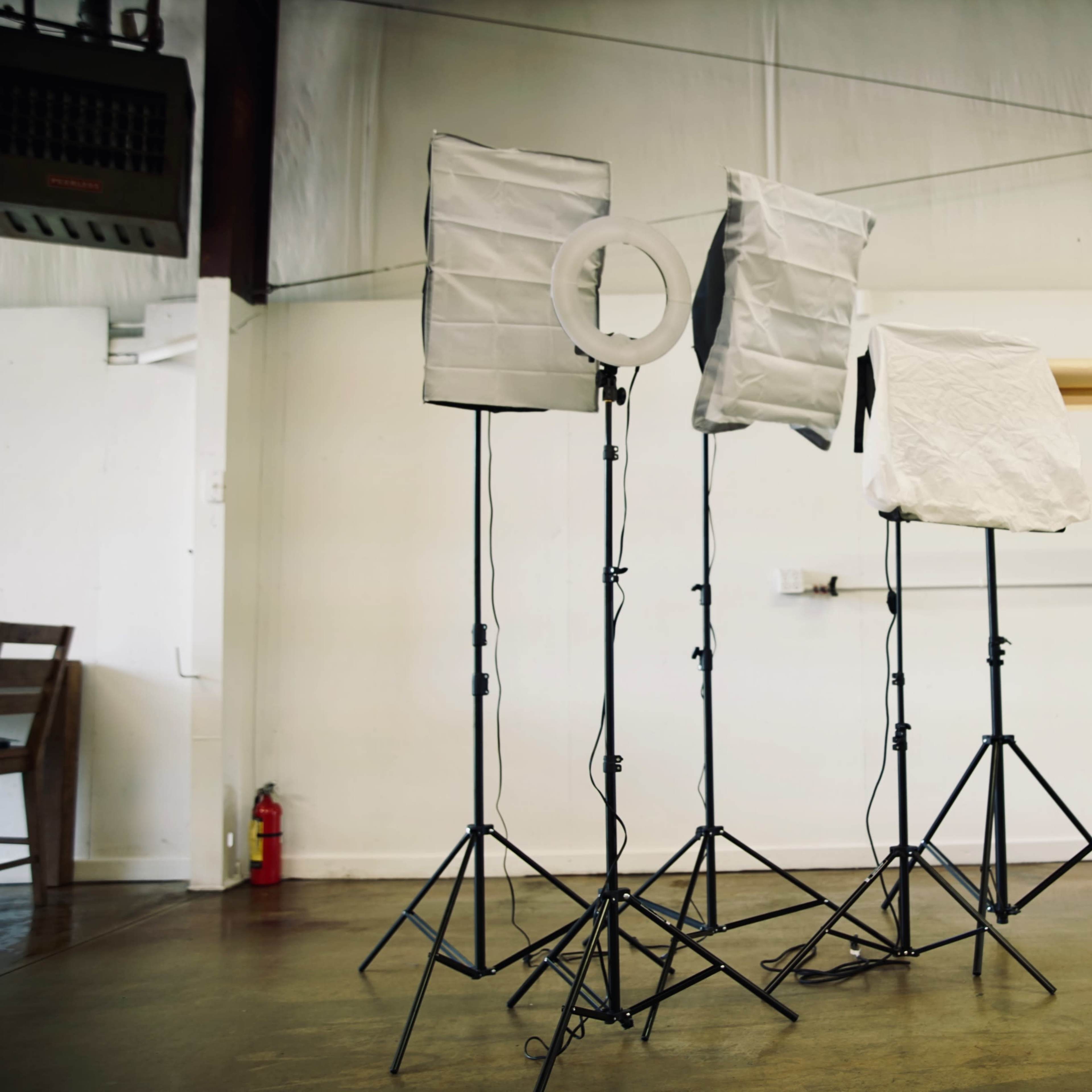 A set of photography lighting equipment is arranged on tripods in a studio with a plain background.